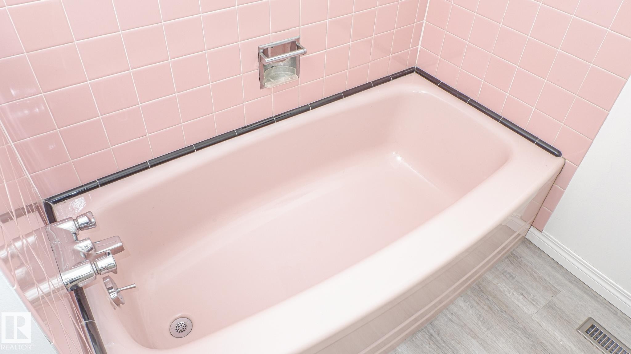 Bathtub with pink subway tile surround, dark tile trim, chrome fixtures, and wood-finish flooring - 11131 52 Street, Edmonton, AB - Indoor Photo Showing Bathroom