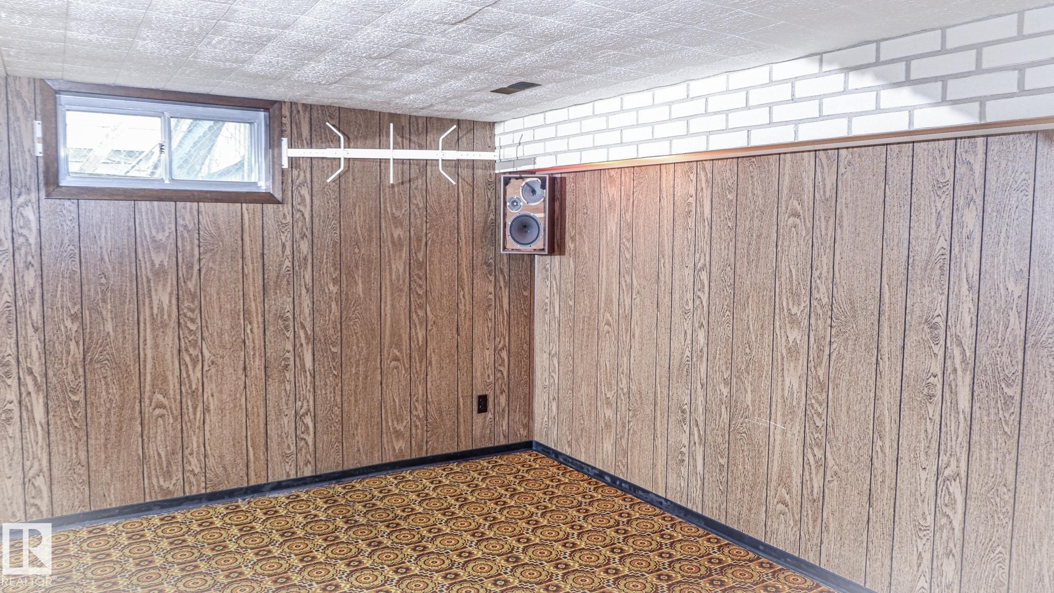 Recreation room featuring wood paneling, white brick accent, geometric pattern carpet, and acoustic ceiling tiles - 11131 52 Street, Edmonton, AB - Indoor Photo Showing Other Room