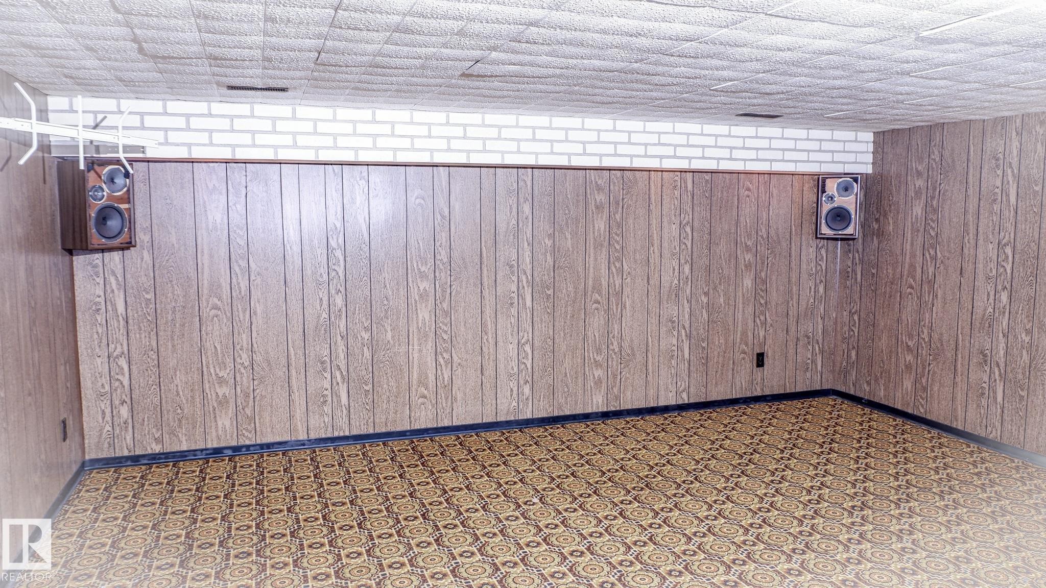Recreation room featuring wood paneling, white brick accent, geometric pattern carpet, and acoustic ceiling tiles - 11131 52 Street, Edmonton, AB - Photo Showing Other Room