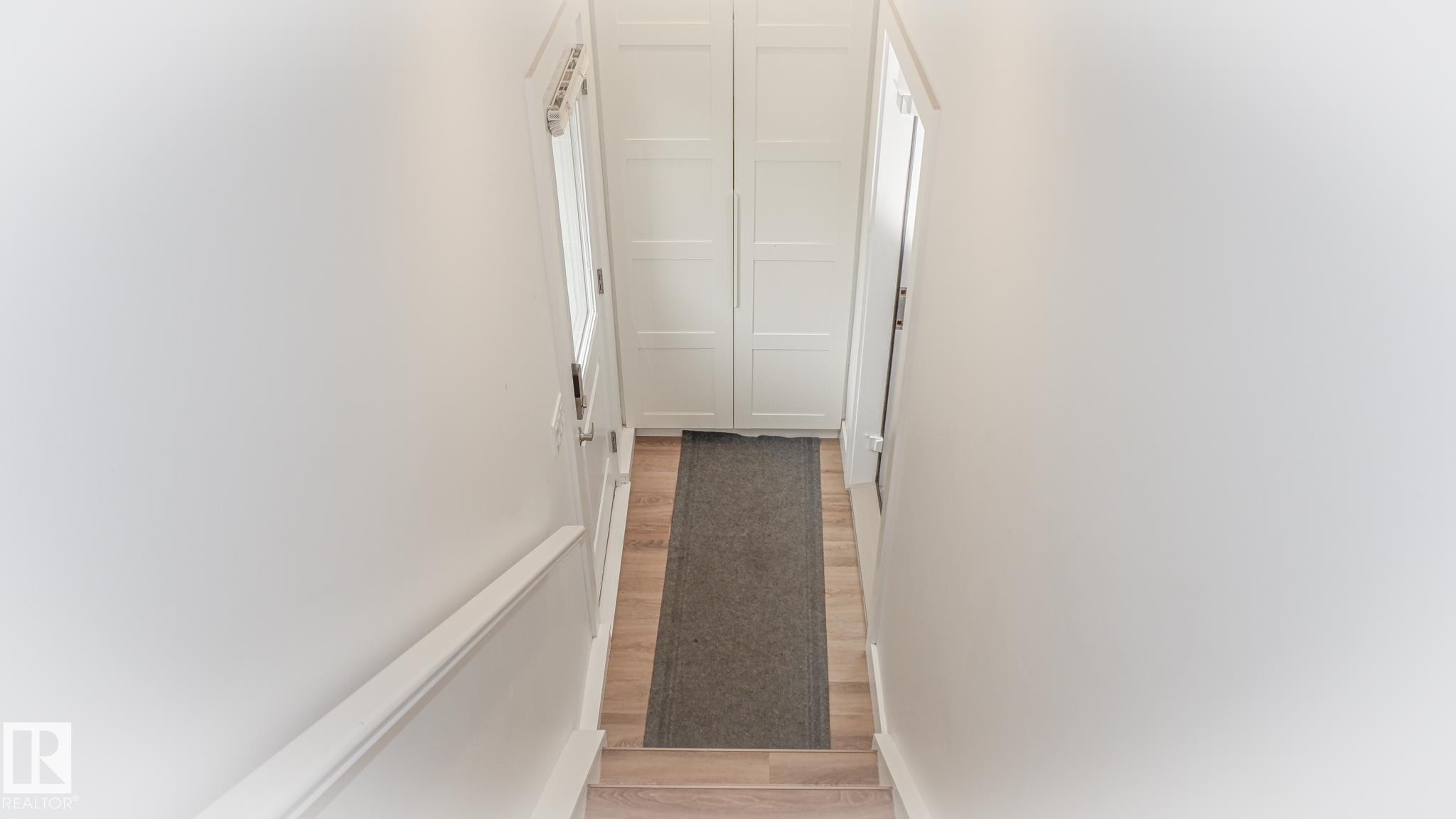 Well-lit hallway featuring light wood-finish flooring, white walls, and a white handrail - 11131 52 Street, Edmonton, AB - Indoor Photo Showing Other Room