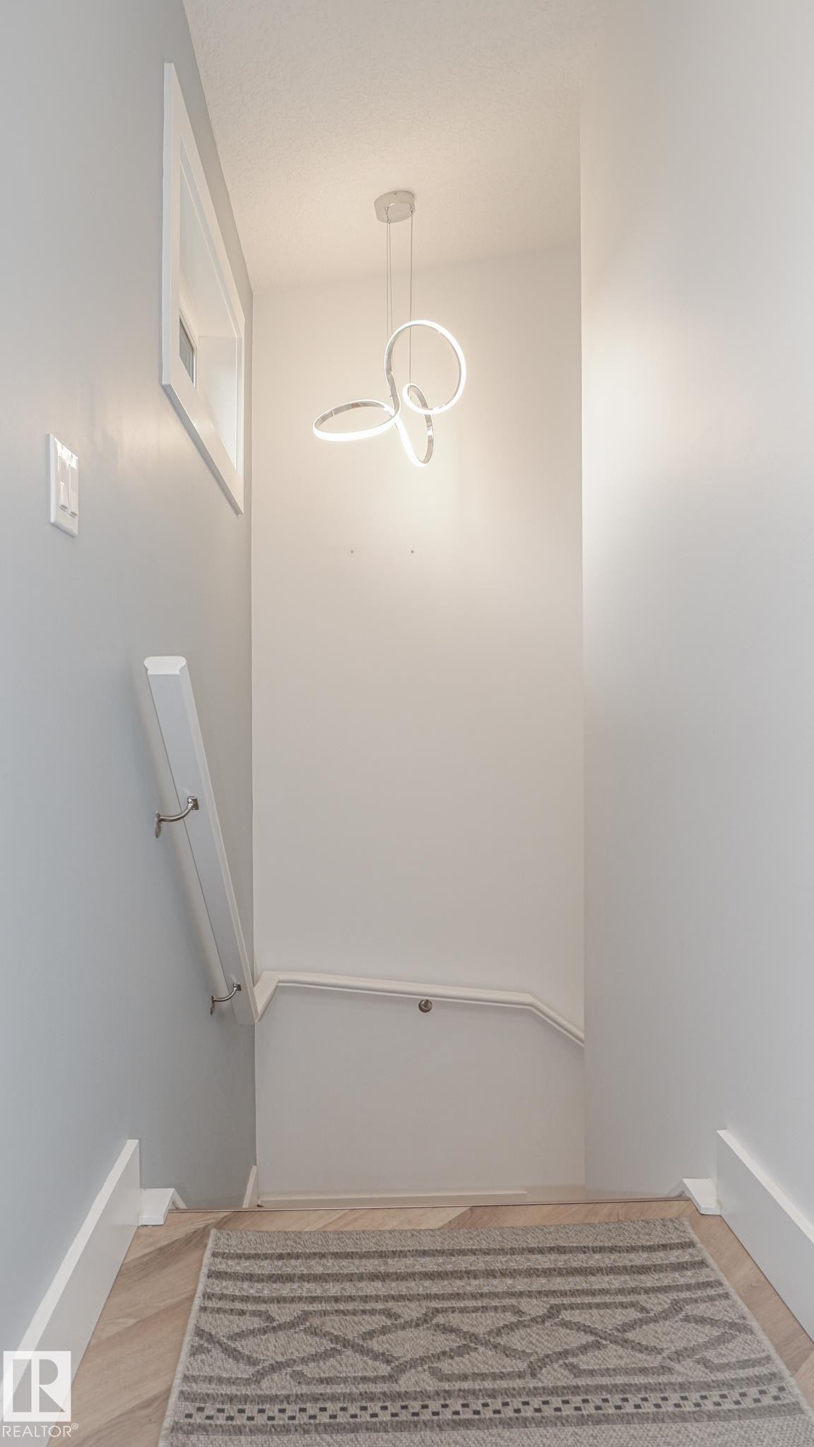Modern pendant light fixture illuminating a stairwell with light wood-finish flooring - 11131 52 Street, Edmonton, AB - Indoor