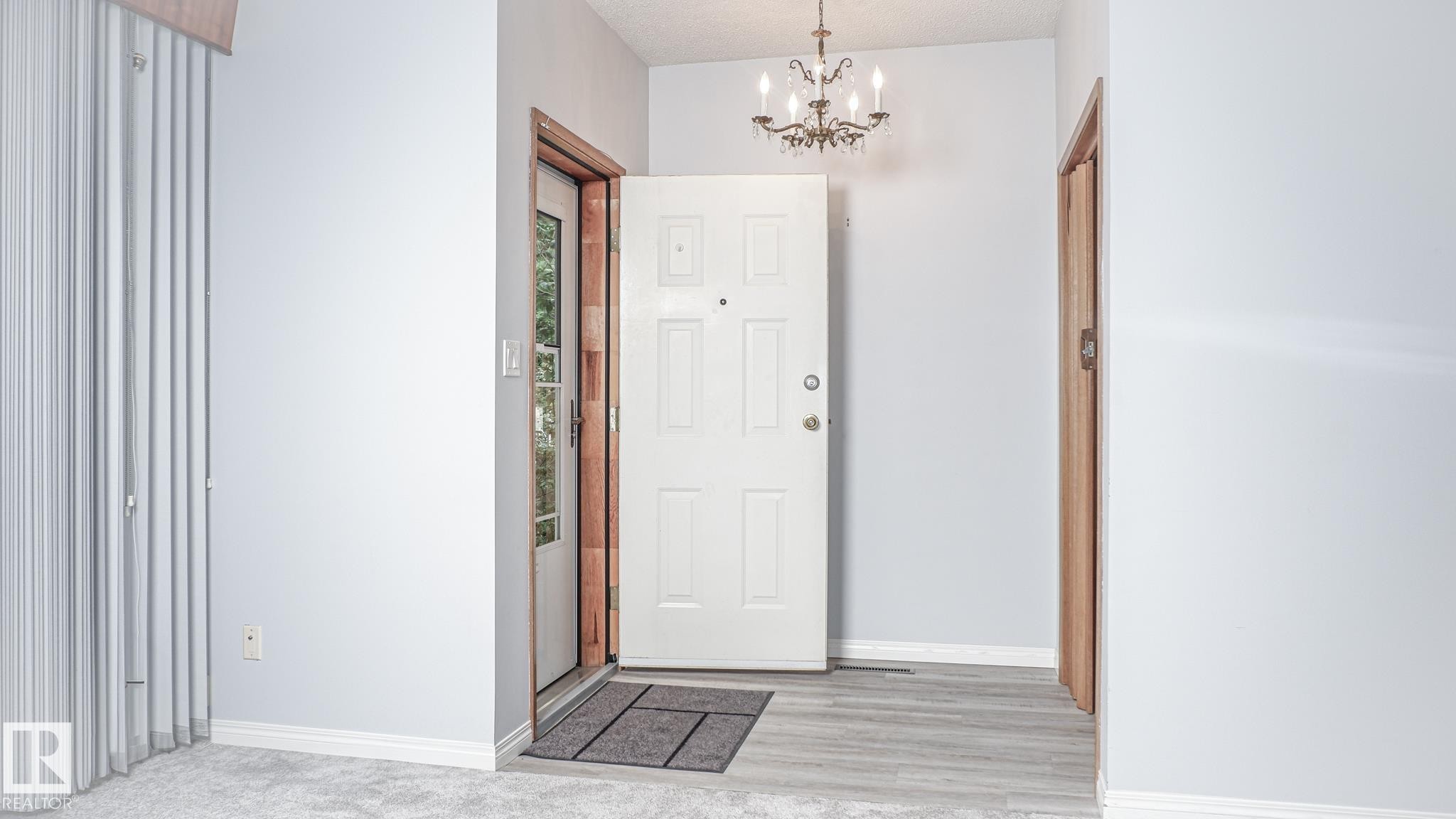 Entryway featuring a decorative chandelier, white paneled door, wood-finish flooring, and white baseboards - 11131 52 Street, Edmonton, AB - Indoor Photo Showing Other Room