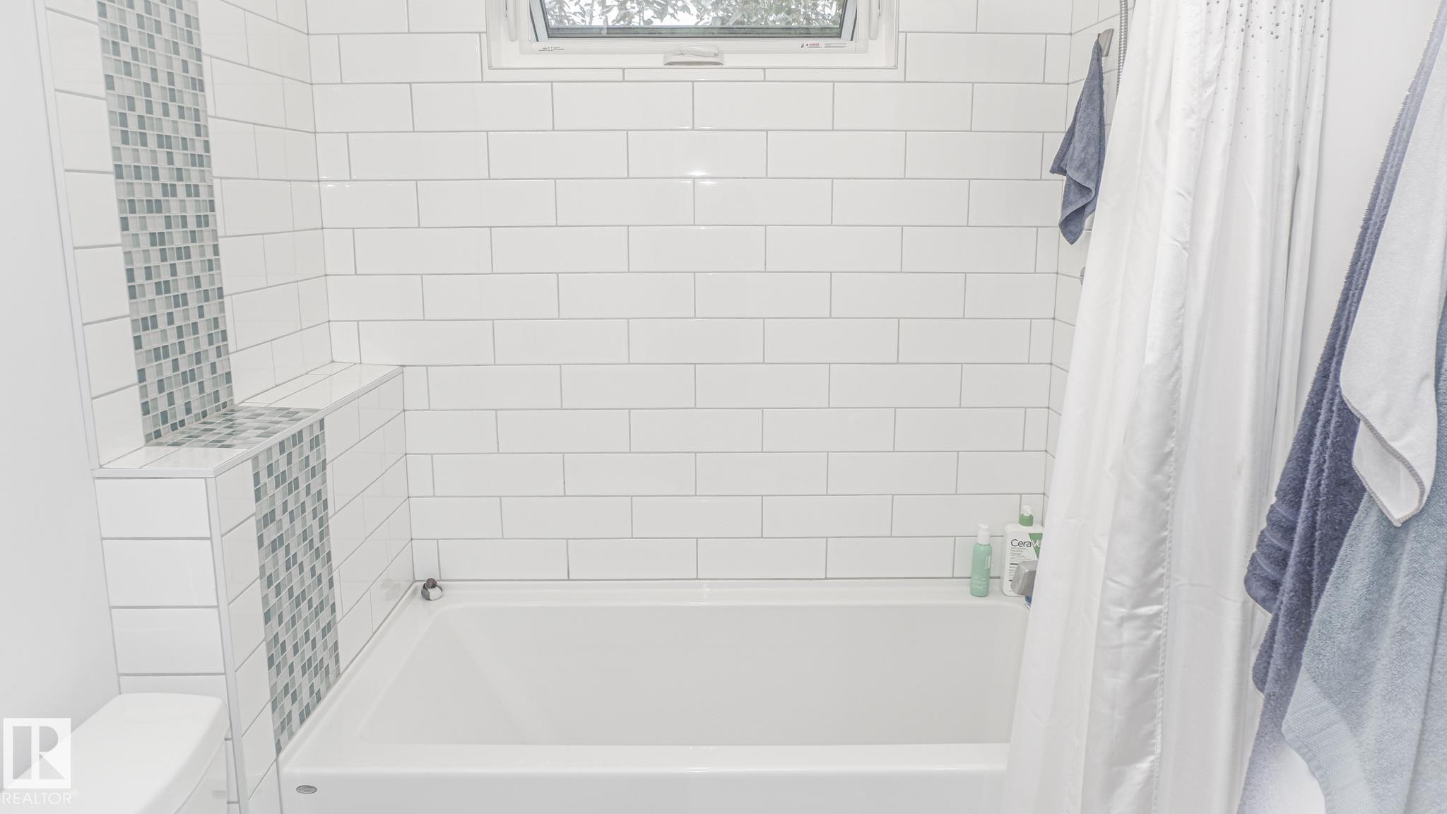 White subway tile surround in a full bathroom, featuring an integrated tub, a mosaic tile accent strip, and a high-set horizontal window - 11131 52 Street, Edmonton, AB - Indoor Photo Showing Bathroom