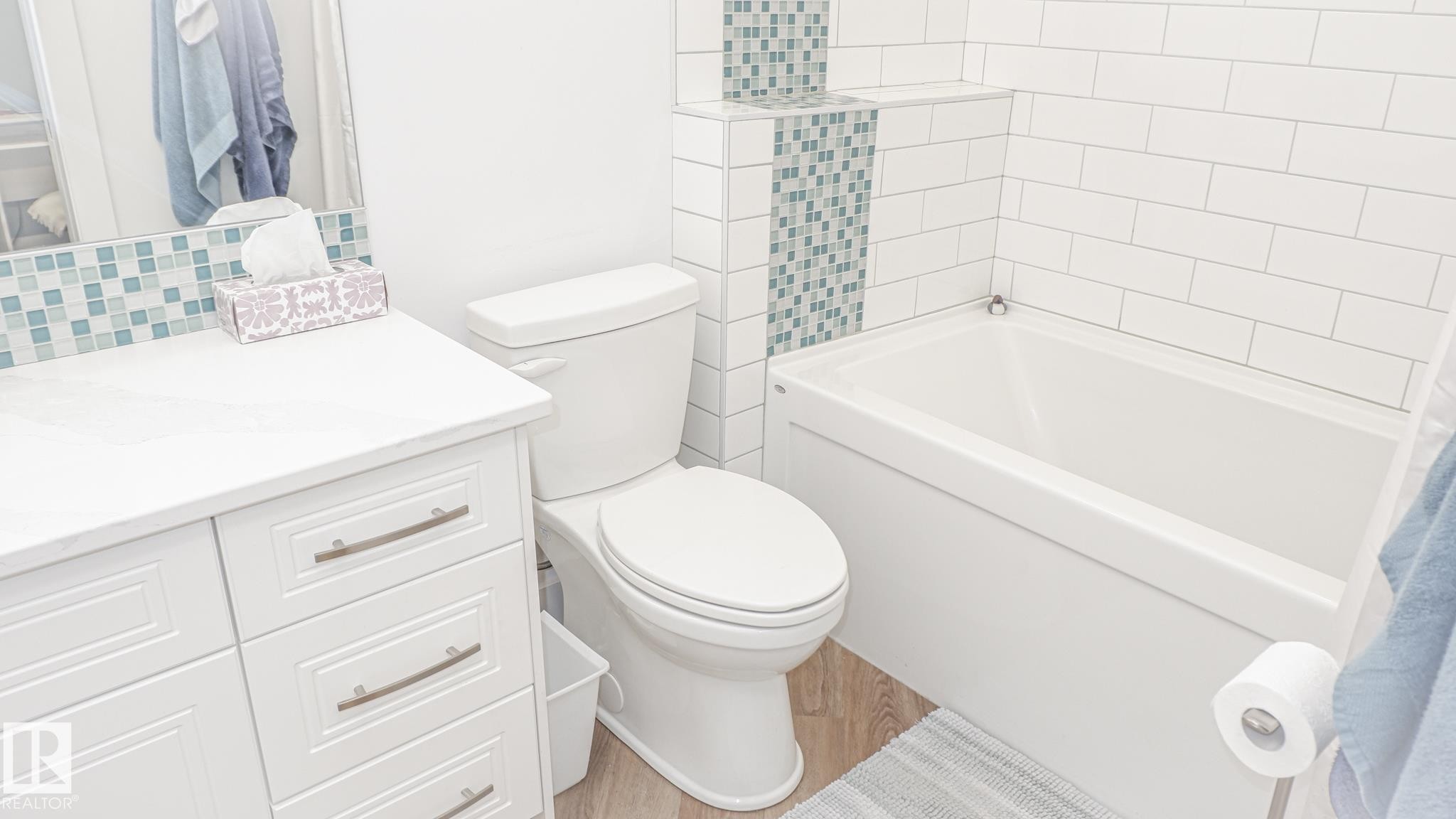 Modern bathroom featuring a white vanity with integrated sink, subway tile accents, patterned mosaic tile, a white toilet, and a built-in bathtub - 11131 52 Street, Edmonton, AB - Indoor Photo Showing Bathroom