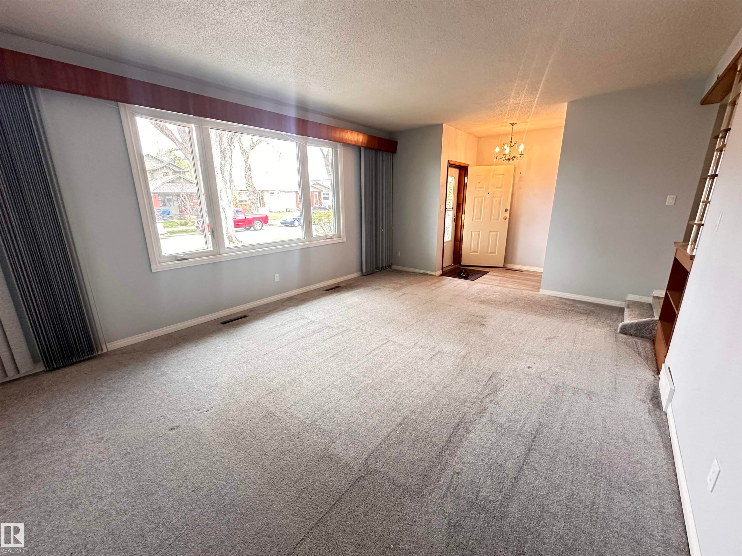 Living area featuring light grey walls, grey carpeting, a large bay window with white trim, and a wood-finish pelmet - 11131 52 Street, Edmonton, AB - Indoor Photo Showing Other Room
