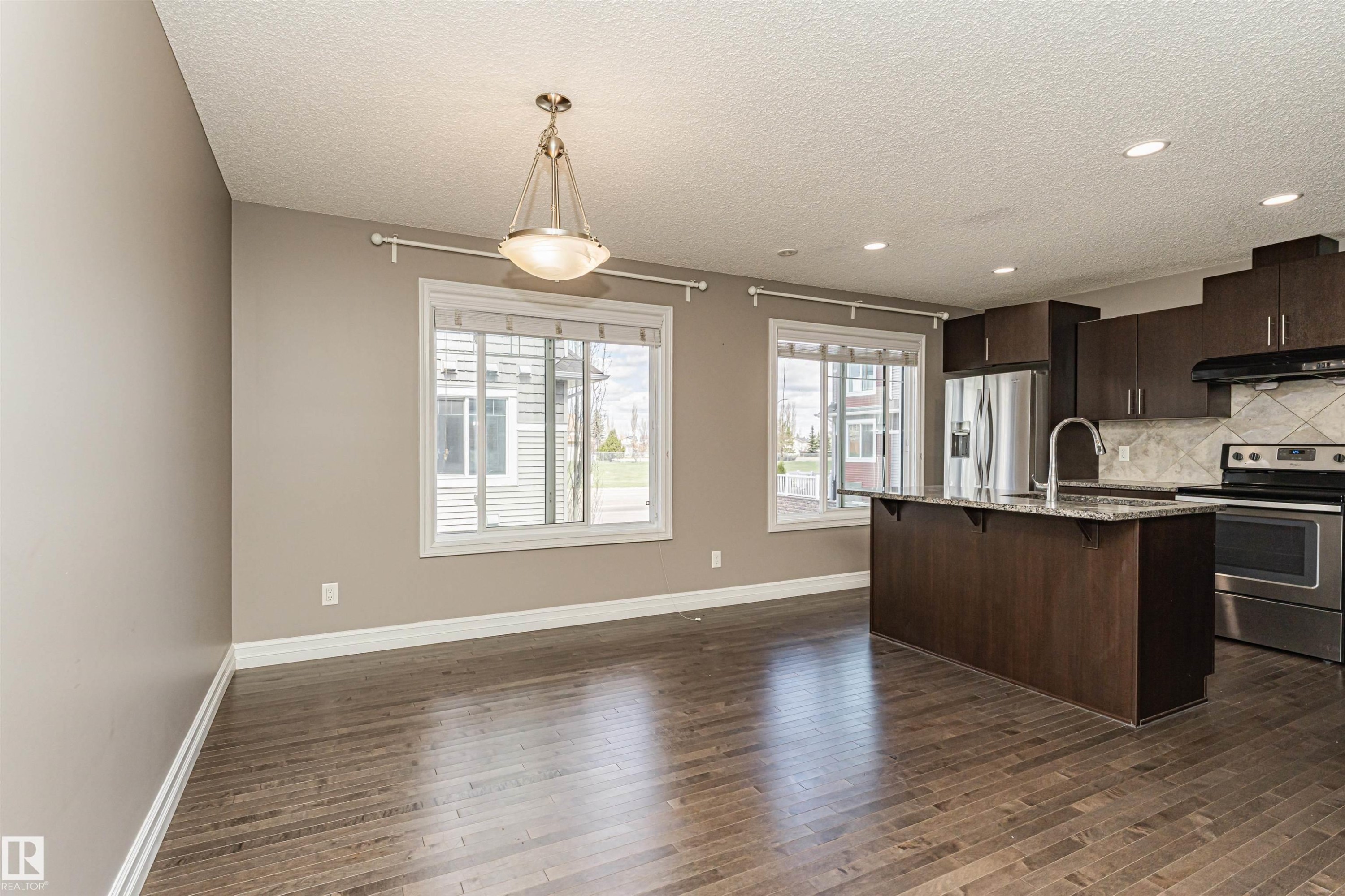 Open-concept living area featuring wood-finish flooring and ample natural light from two windows - #110 3625 144 Av Nw, Edmonton, AB - Indoor Photo Showing Kitchen