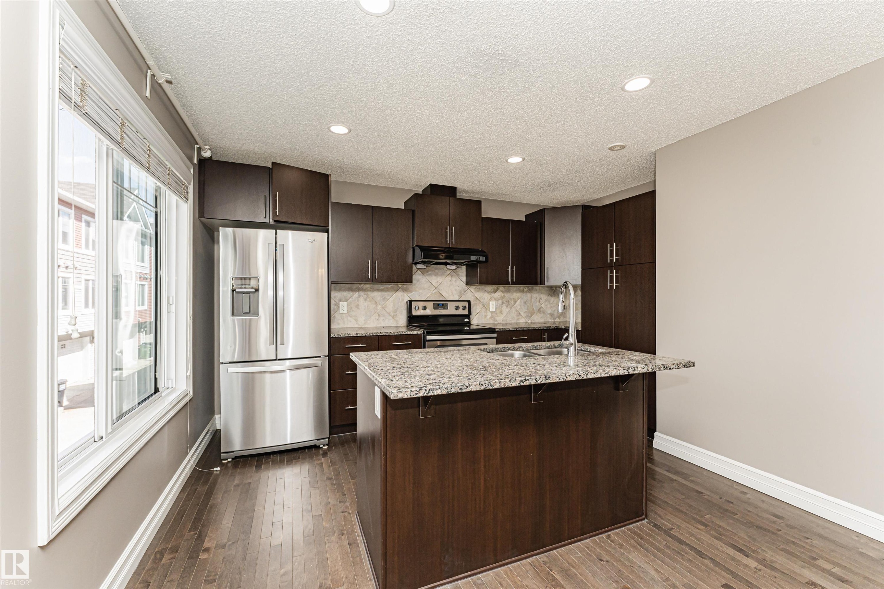 Kitchen featuring dark wood-finish cabinetry, stainless steel appliances, granite countertops, and wood-finish flooring - #110 3625 144 Av Nw, Edmonton, AB - Indoor Photo Showing Kitchen