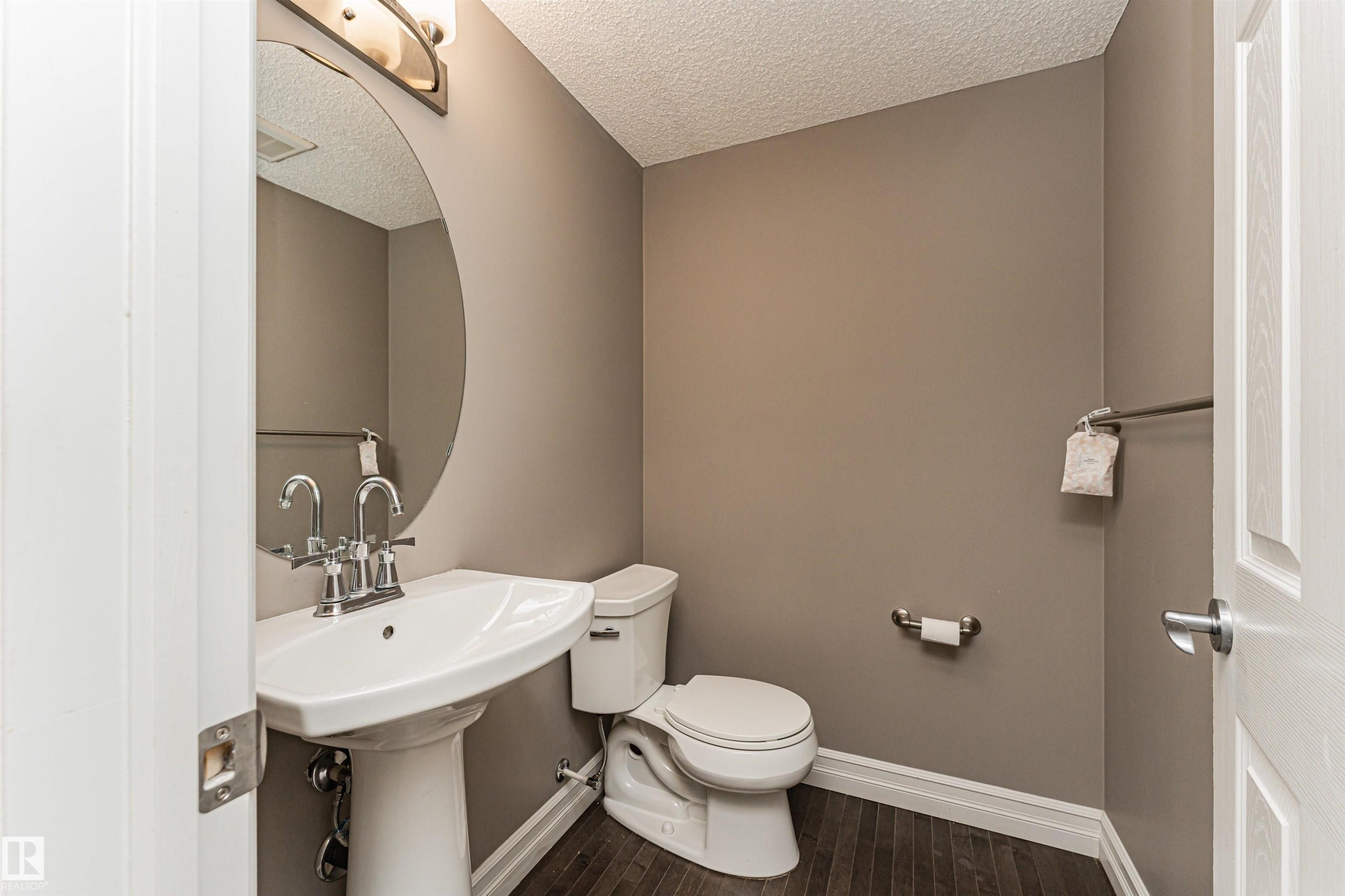 Pedestal sink with chrome fixtures, oval mirror, and wall-mounted light fixture - #110 3625 144 Av Nw, Edmonton, AB - Indoor Photo Showing Bathroom