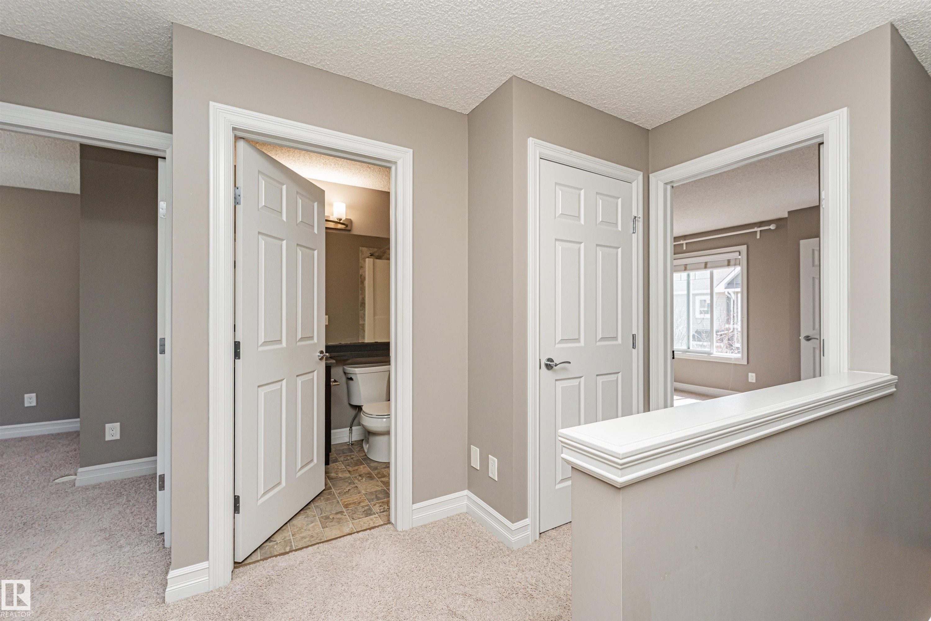 Carpeted hallway featuring a neutral color palette, white trim, and doors with brushed chrome hardware - #110 3625 144 Av Nw, Edmonton, AB - Indoor Photo Showing Other Room