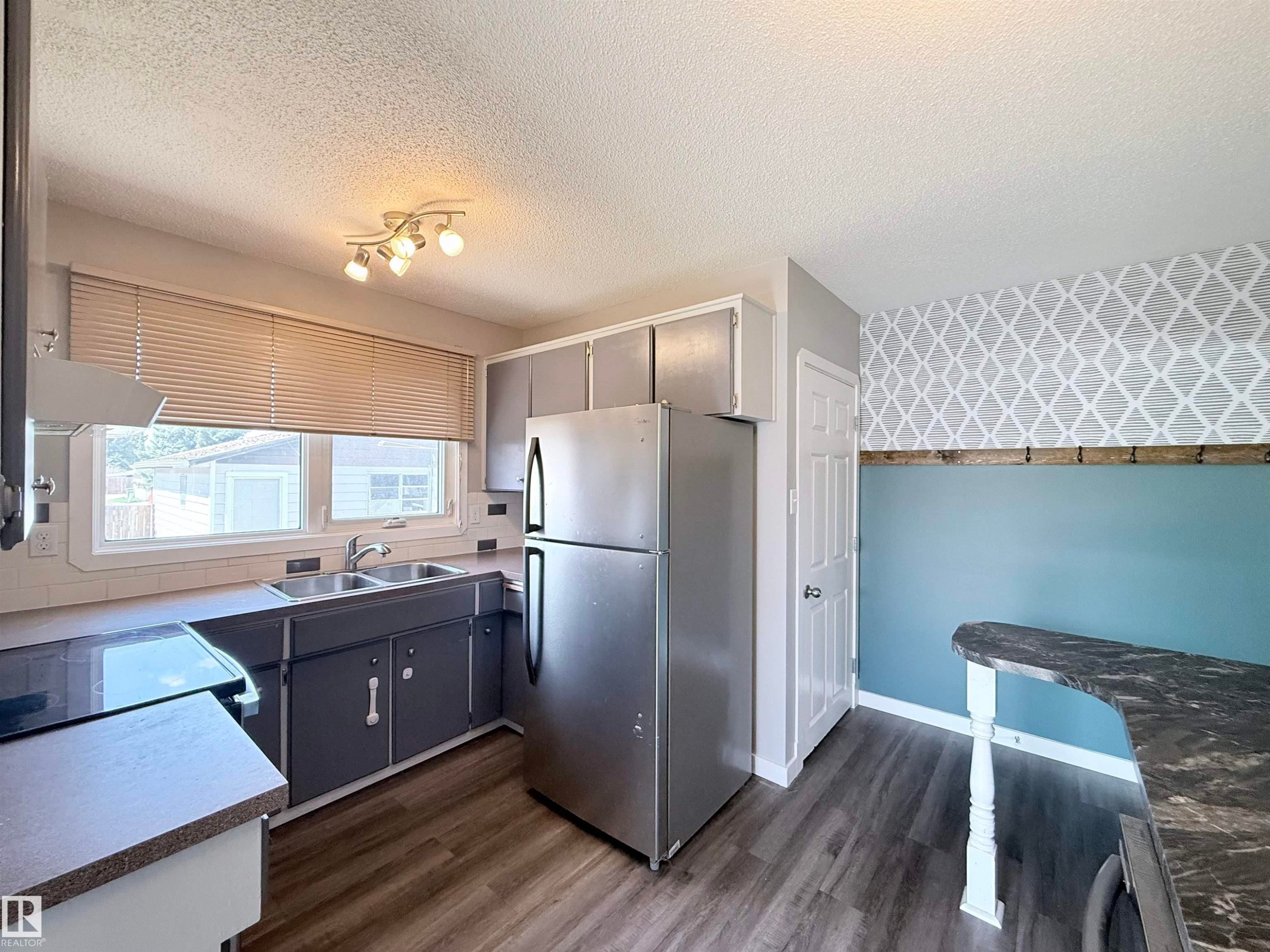 Kitchen featuring stainless steel refrigerator, white tile backsplash, a double basin sink, and wood-finish flooring - 3912 108 Street, Edmonton, AB - Indoor Photo Showing Kitchen With Double Sink