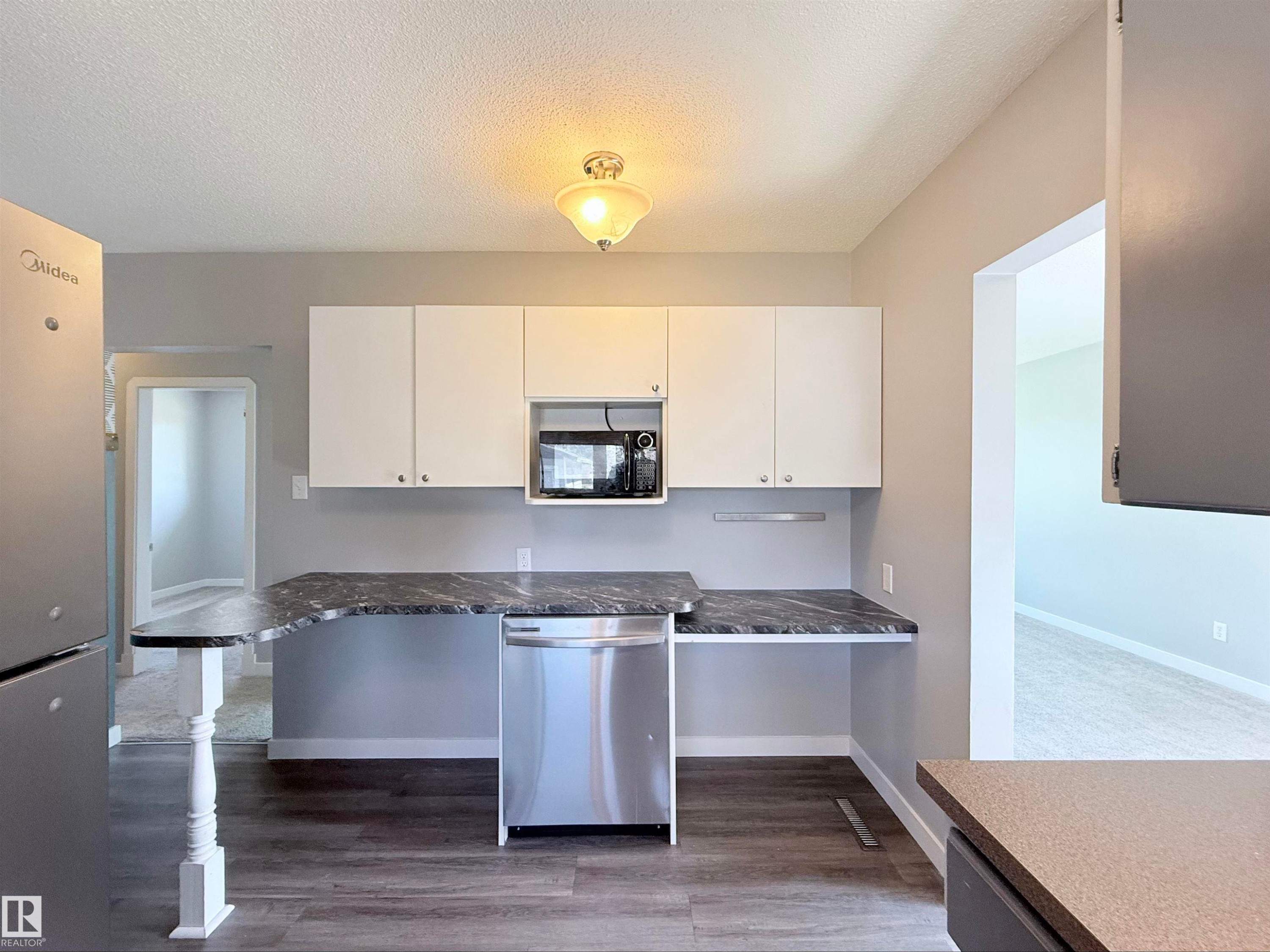 Kitchen featuring white upper cabinetry, dark wood-finish flooring, marbled countertops, and a stainless steel dishwasher - 3912 108 Street, Edmonton, AB - Indoor Photo Showing Kitchen