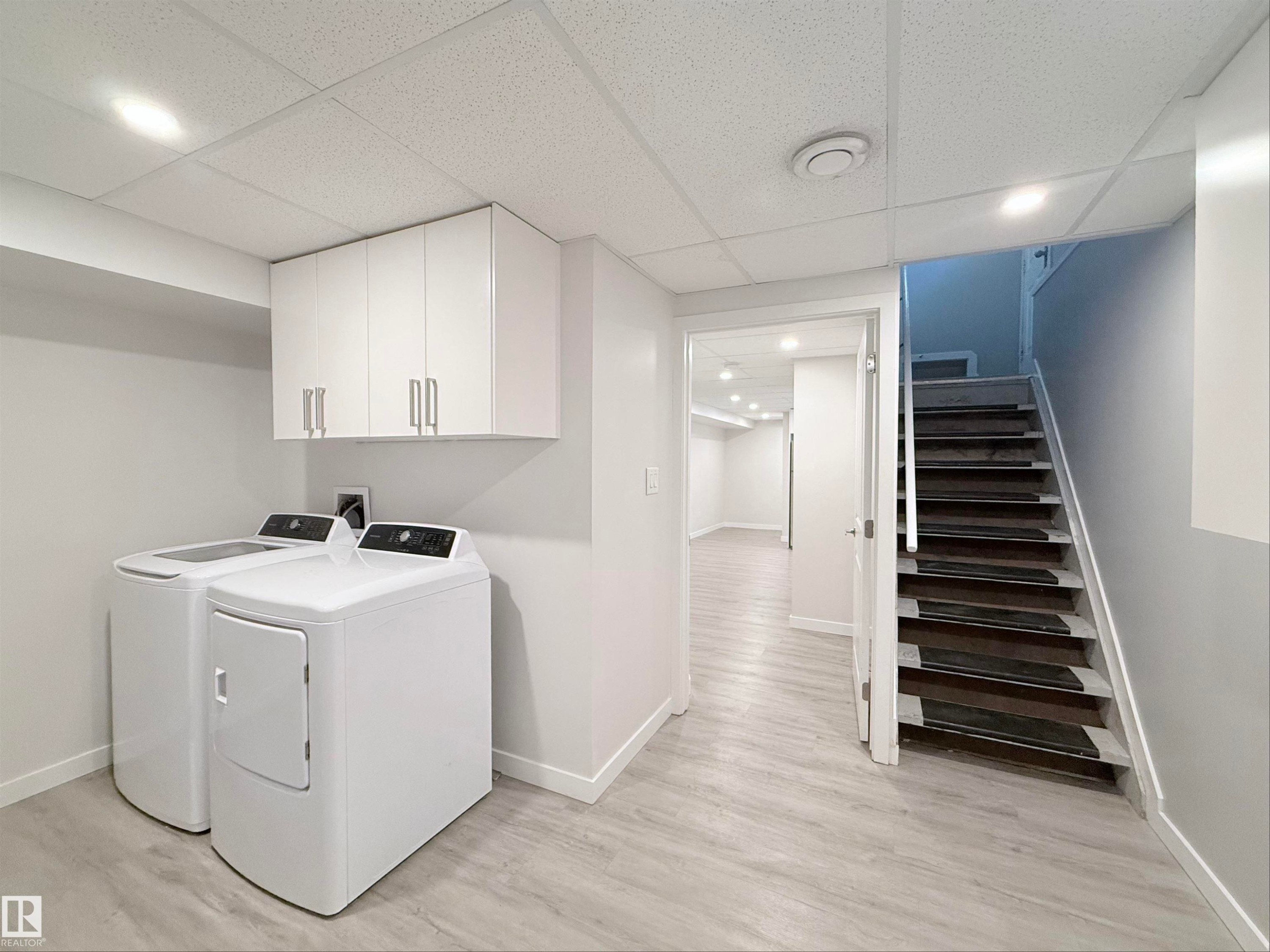 Dedicated laundry area featuring a washer and dryer, light wood-finish flooring, white wall cabinetry with brushed nickel hardware, and a drop ceiling with recessed lighting - 3912 108 Street, Edmonton, AB - Indoor Photo Showing Laundry Room