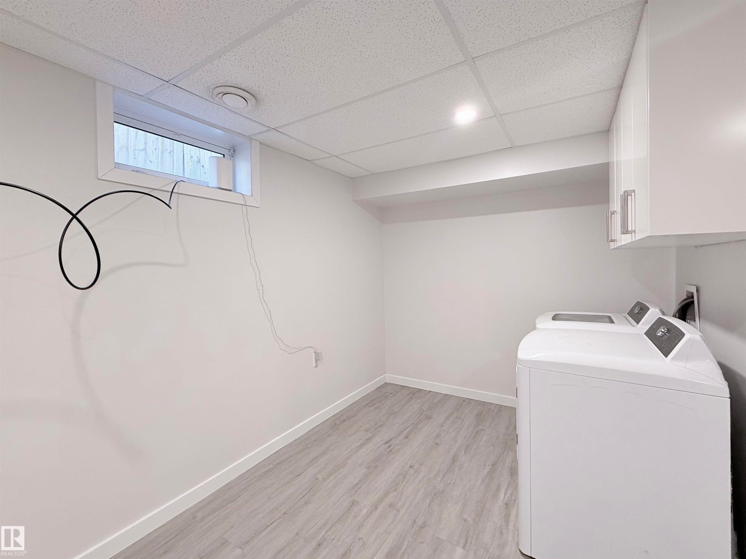 Dedicated laundry area featuring a drop ceiling with recessed lighting, light wood-finish flooring, white baseboards, and a window for natural light - 3912 108 Street, Edmonton, AB - Indoor Photo Showing Laundry Room