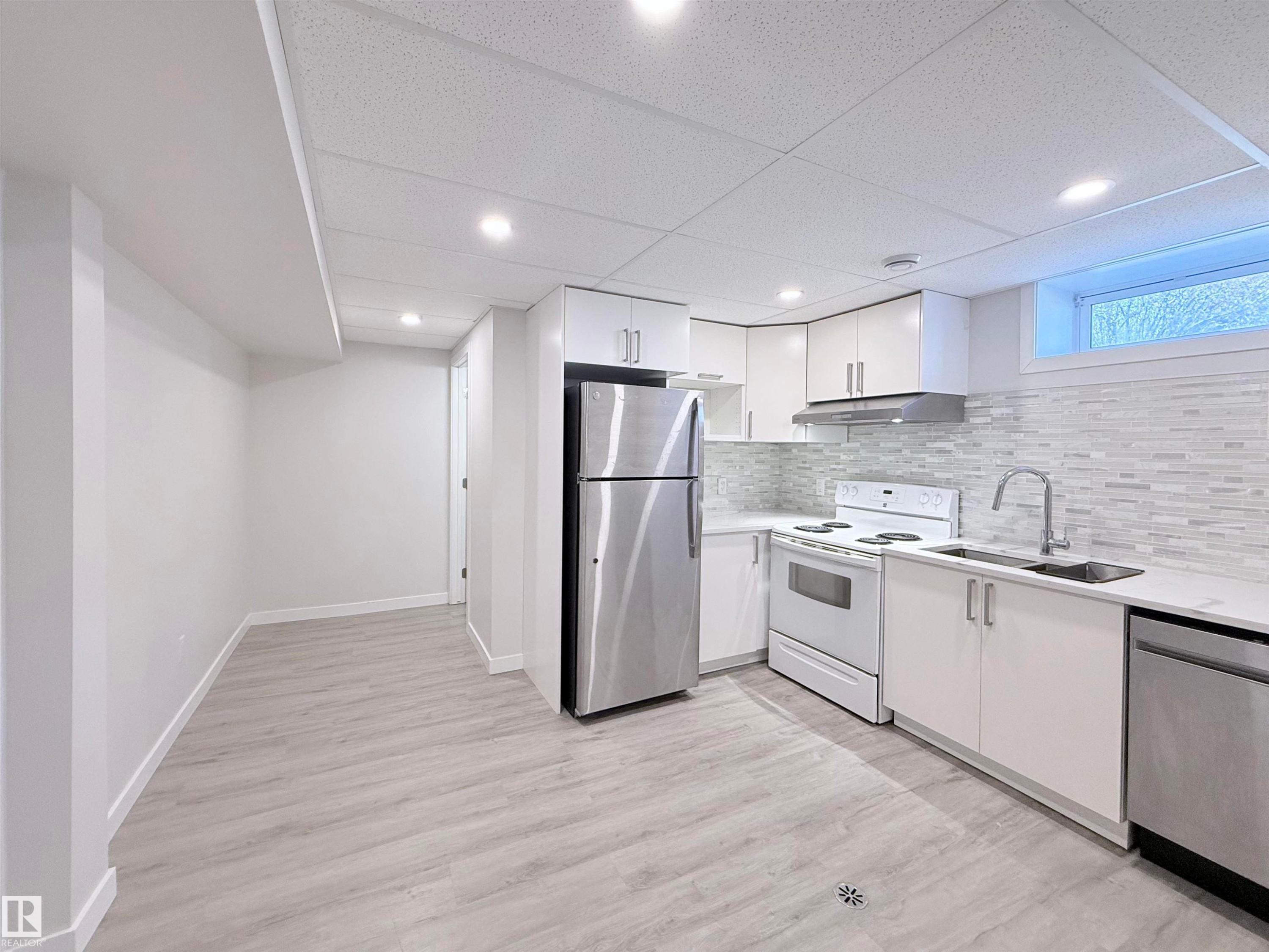 Modern kitchen featuring white cabinetry, stainless steel refrigerator and dishwasher, white electric range, and a mosaic tile backsplash - 3912 108 Street, Edmonton, AB - Indoor Photo Showing Kitchen