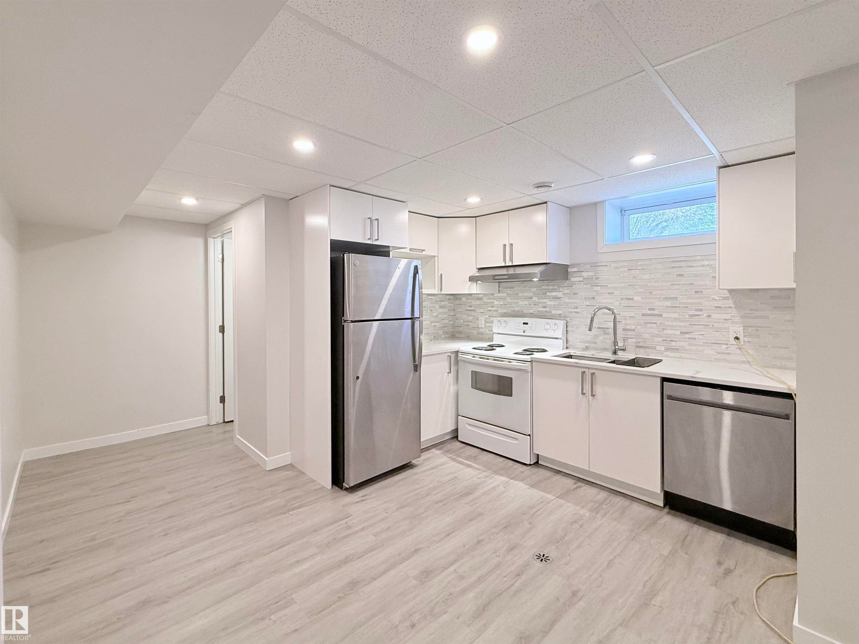Modern kitchen featuring white cabinetry, light-toned countertops, and a full suite of appliances including a stainless steel refrigerator and dishwasher - 3912 108 Street, Edmonton, AB - Indoor Photo Showing Kitchen