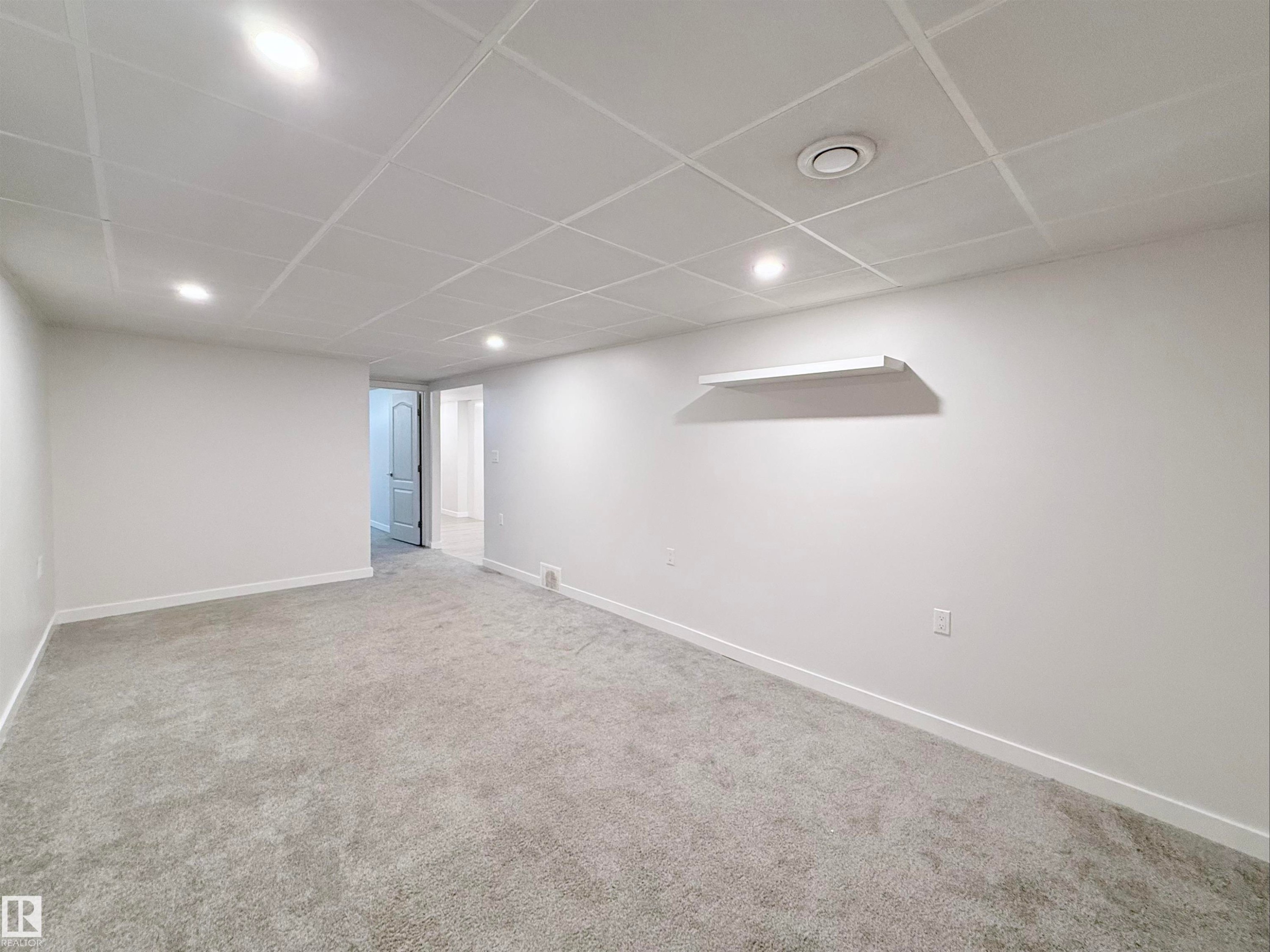 Spacious interior room featuring new gray carpeting, white walls, recessed ceiling lights, a drop ceiling, and a built-in wall shelf - 3912 108 Street, Edmonton, AB - Indoor