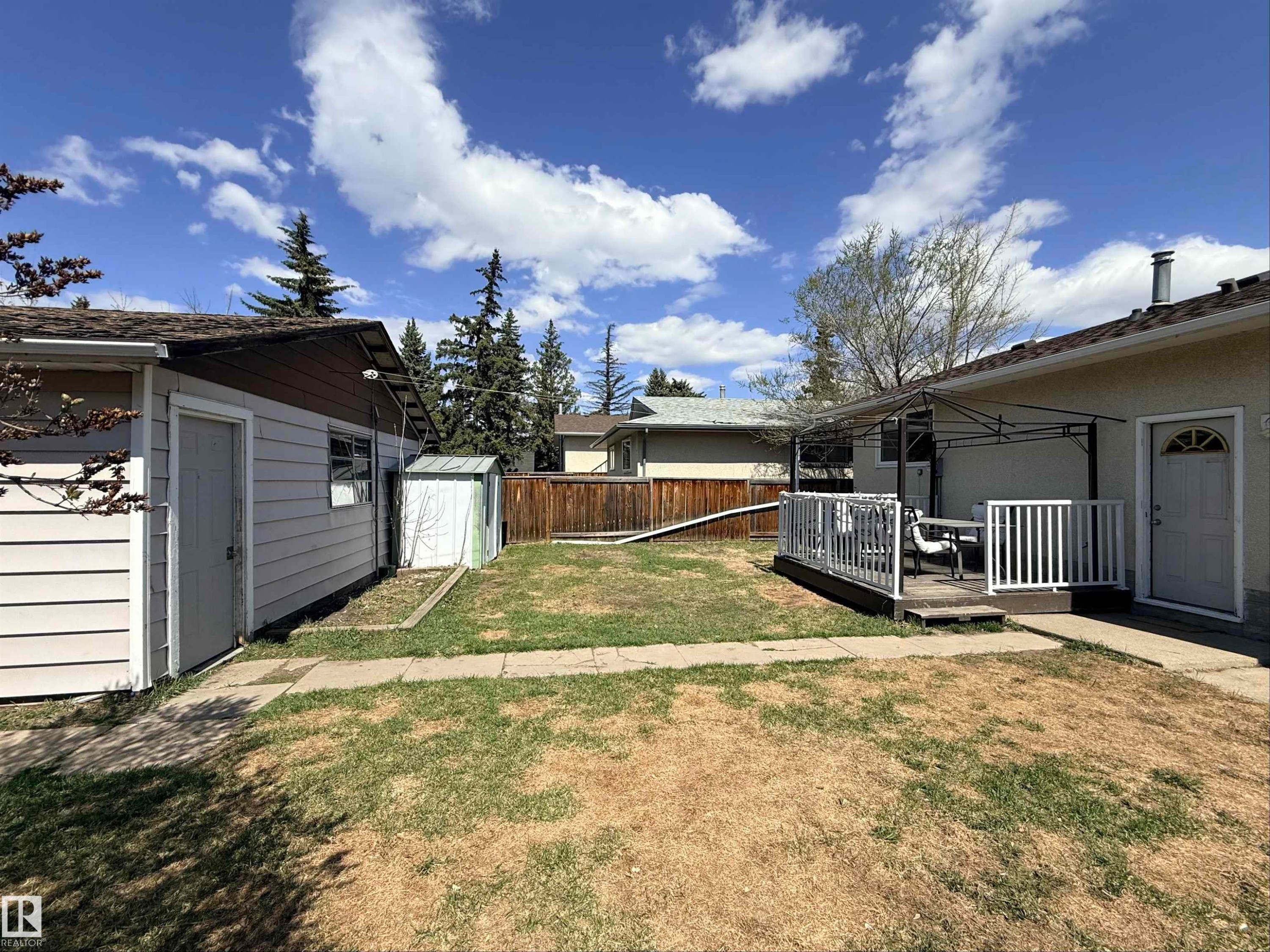Spacious backyard featuring a wood fence, a detached shed, and a raised wooden deck with white railings - 3912 108 Street, Edmonton, AB - Outdoor