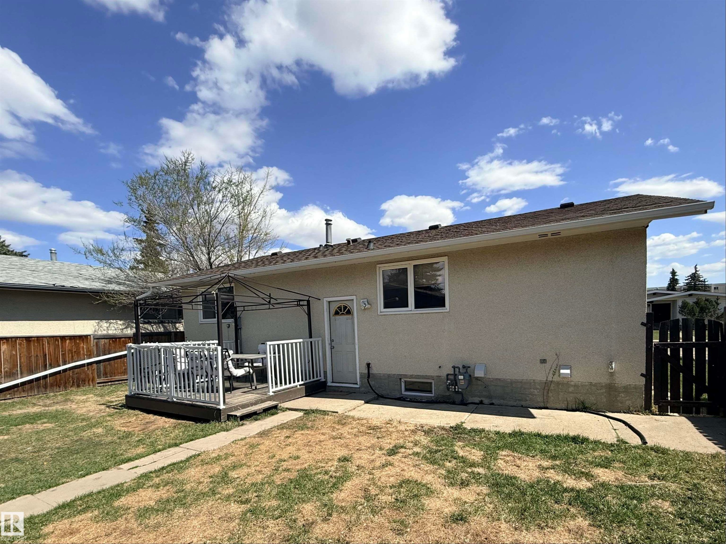 Rear exterior featuring a ground-level wood deck with white railings, stucco siding, and a partial privacy fence - 3912 108 Street, Edmonton, AB - Outdoor