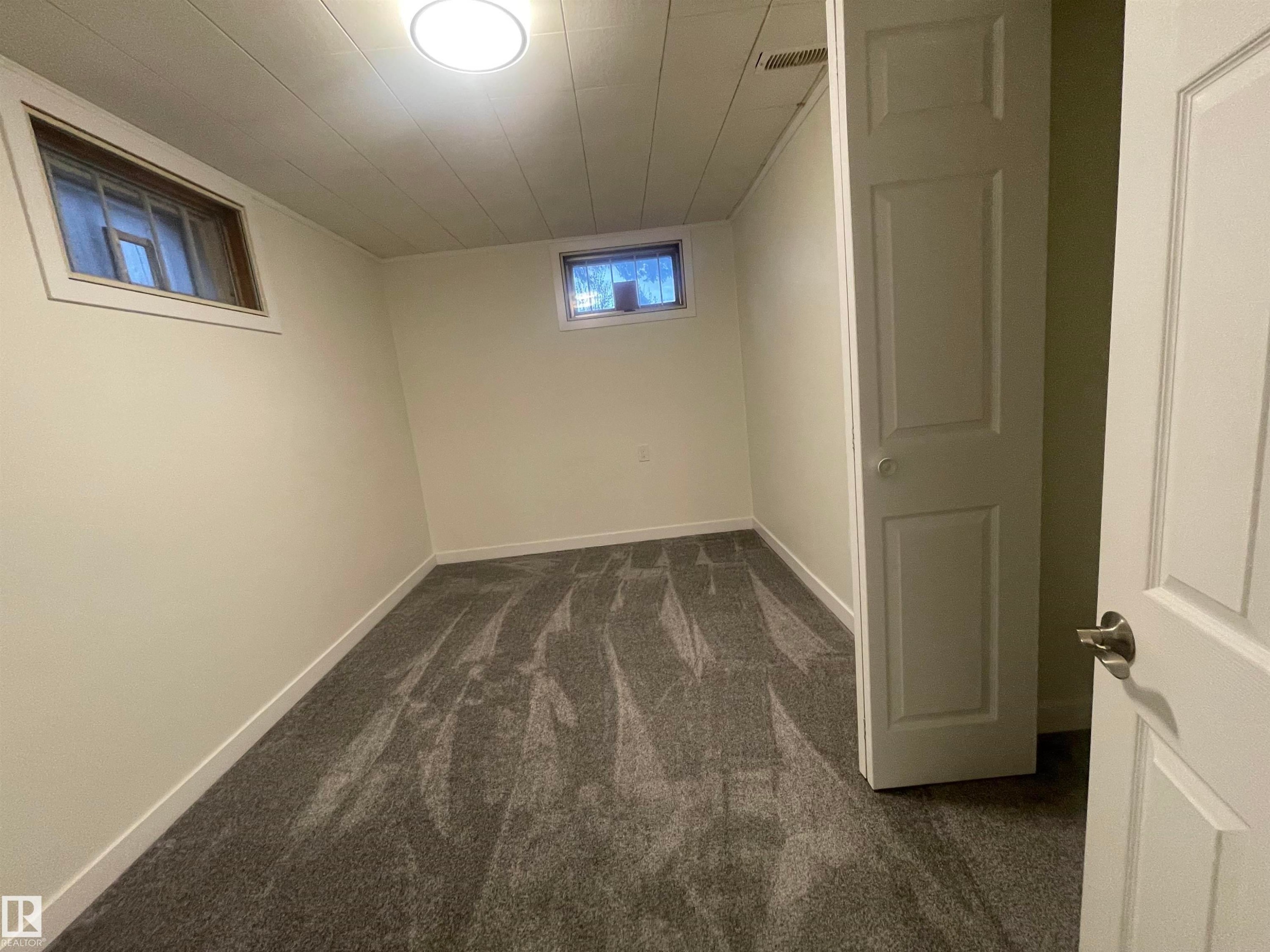 Room featuring new grey patterned carpeting, white walls, two egress windows, a flush-mount ceiling light, and white trim throughout - 13804 132 Avenue, Edmonton, AB - Indoor Photo Showing Other Room