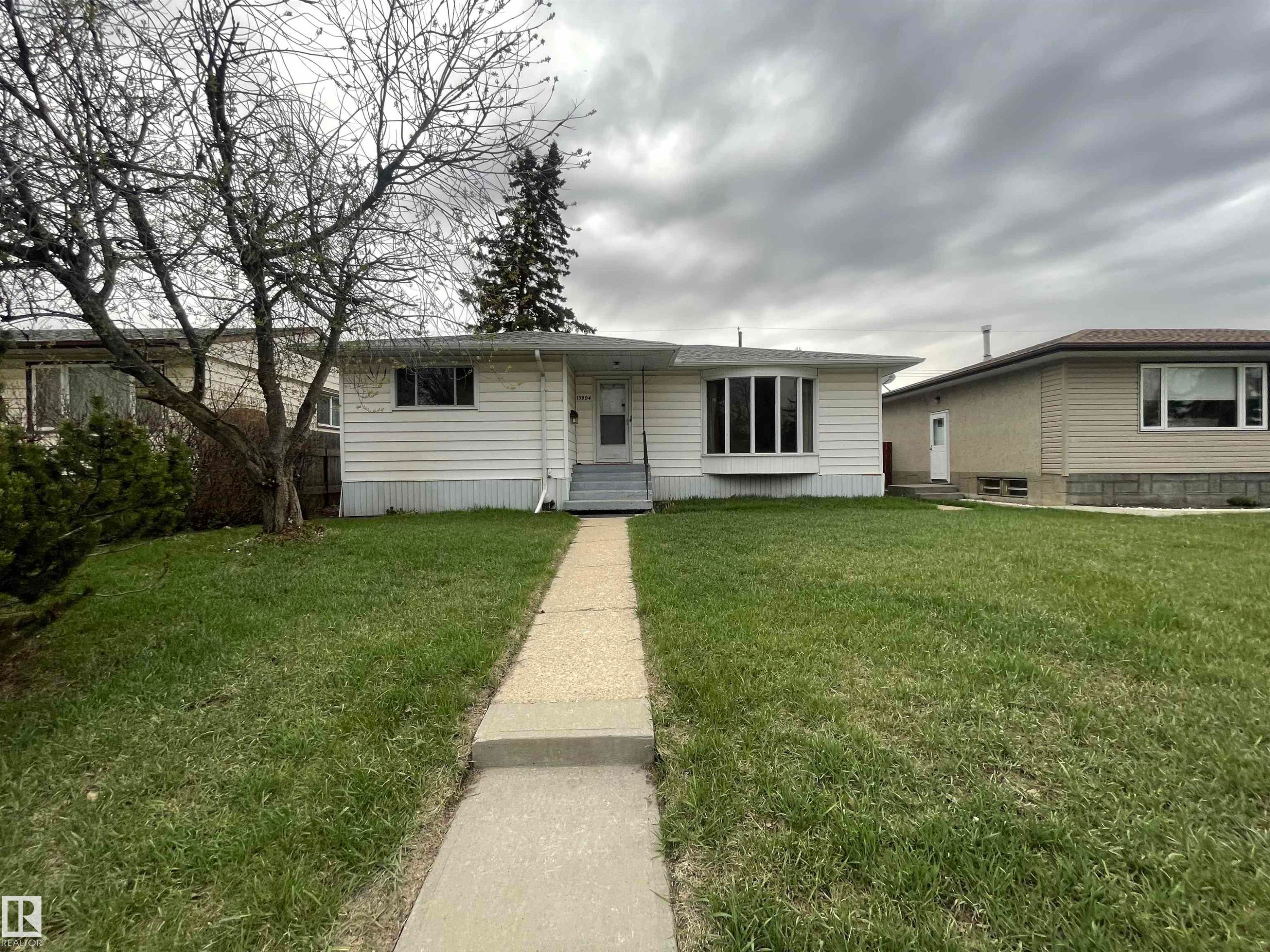 Single-story residence featuring white horizontal siding, a gray concrete walkway, and a front yard with established trees - 13804 132 Avenue, Edmonton, AB - Outdoor