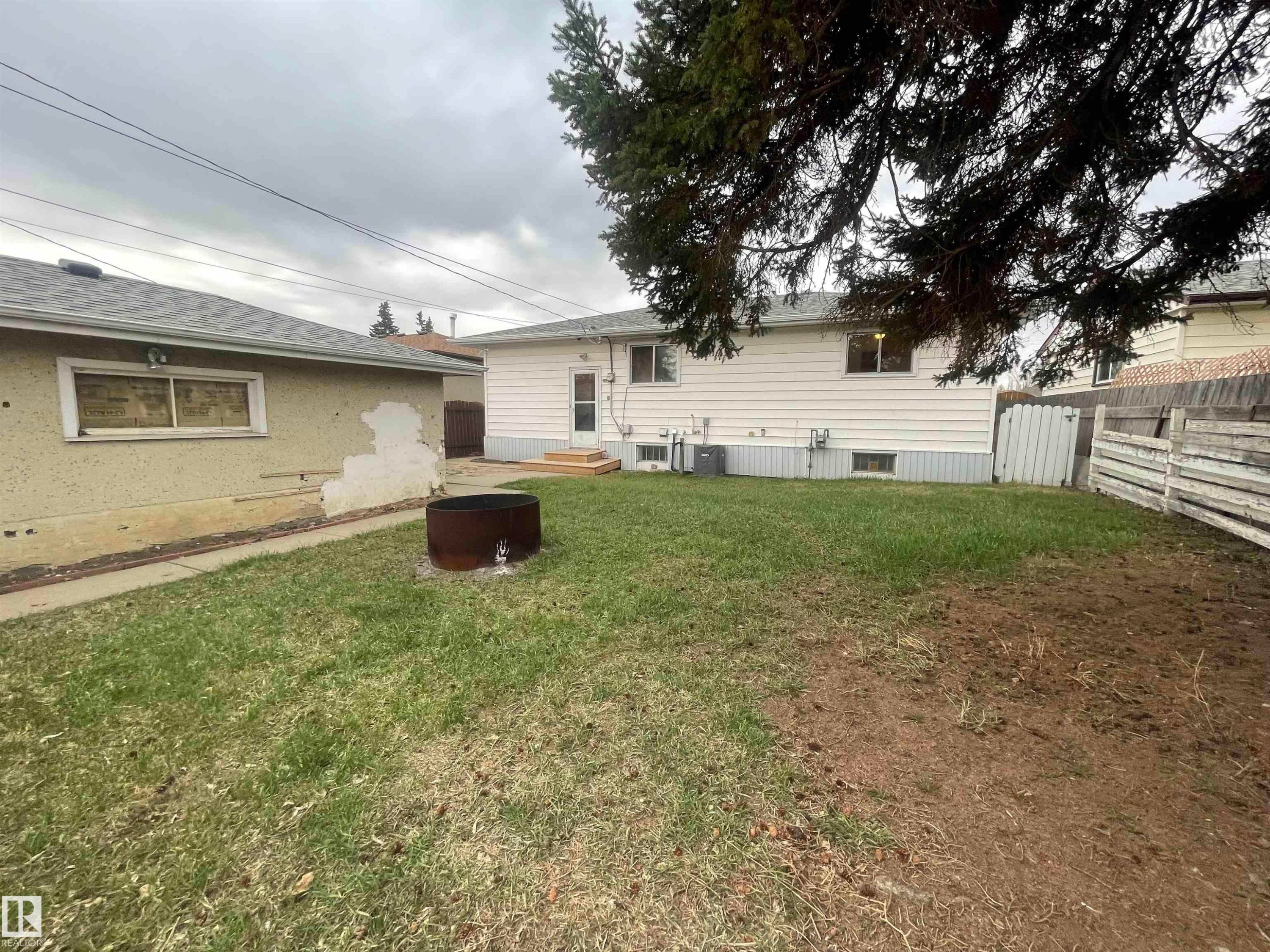 Spacious backyard featuring a white vinyl-sided exterior, a stucco-sided garage, a fire pit, and partial wood fencing - 13804 132 Avenue, Edmonton, AB - Outdoor
