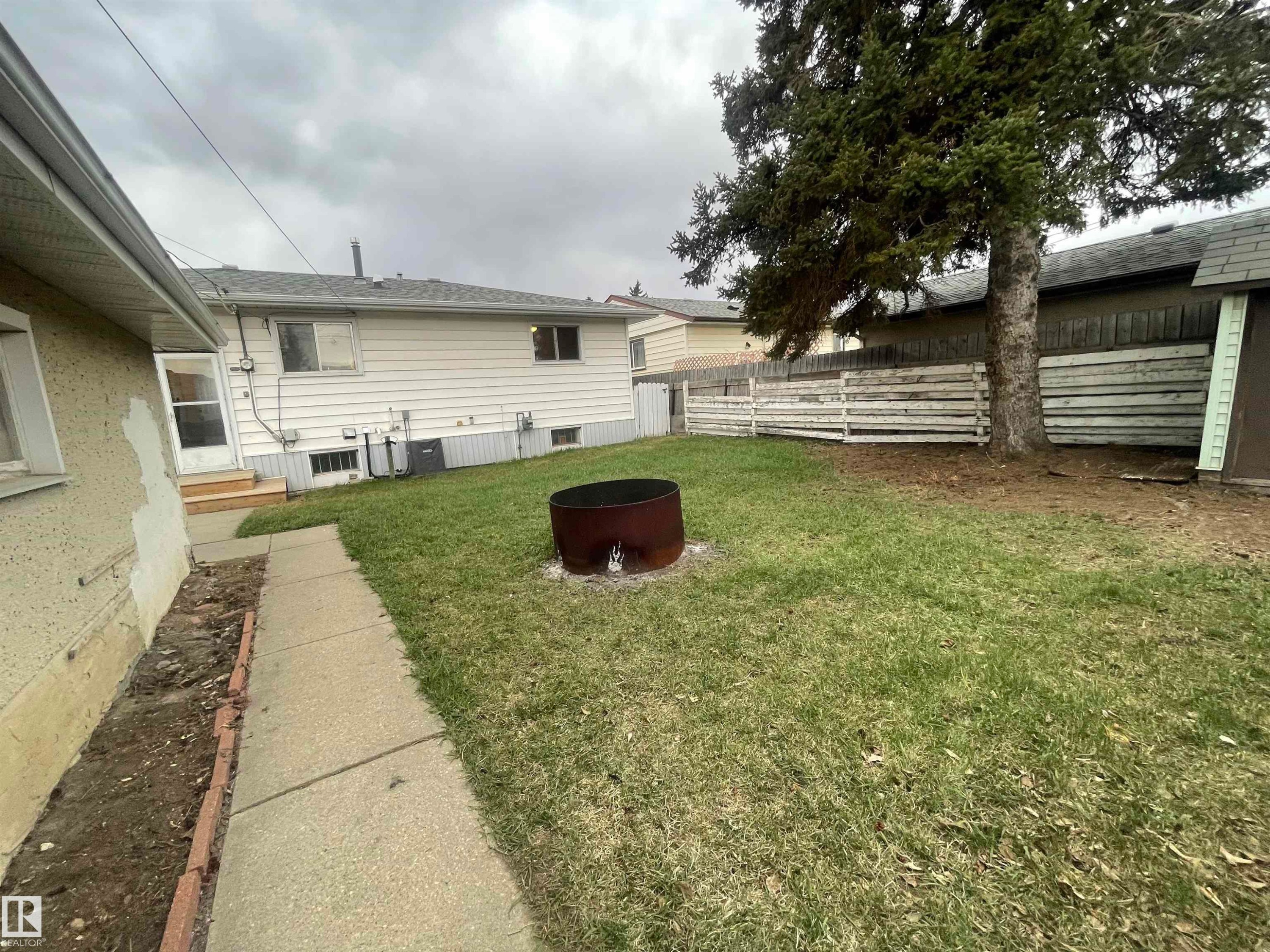 Rear yard featuring a concrete walkway, established tree, wood fencing, and a metal fire pit - 13804 132 Avenue, Edmonton, AB - Outdoor