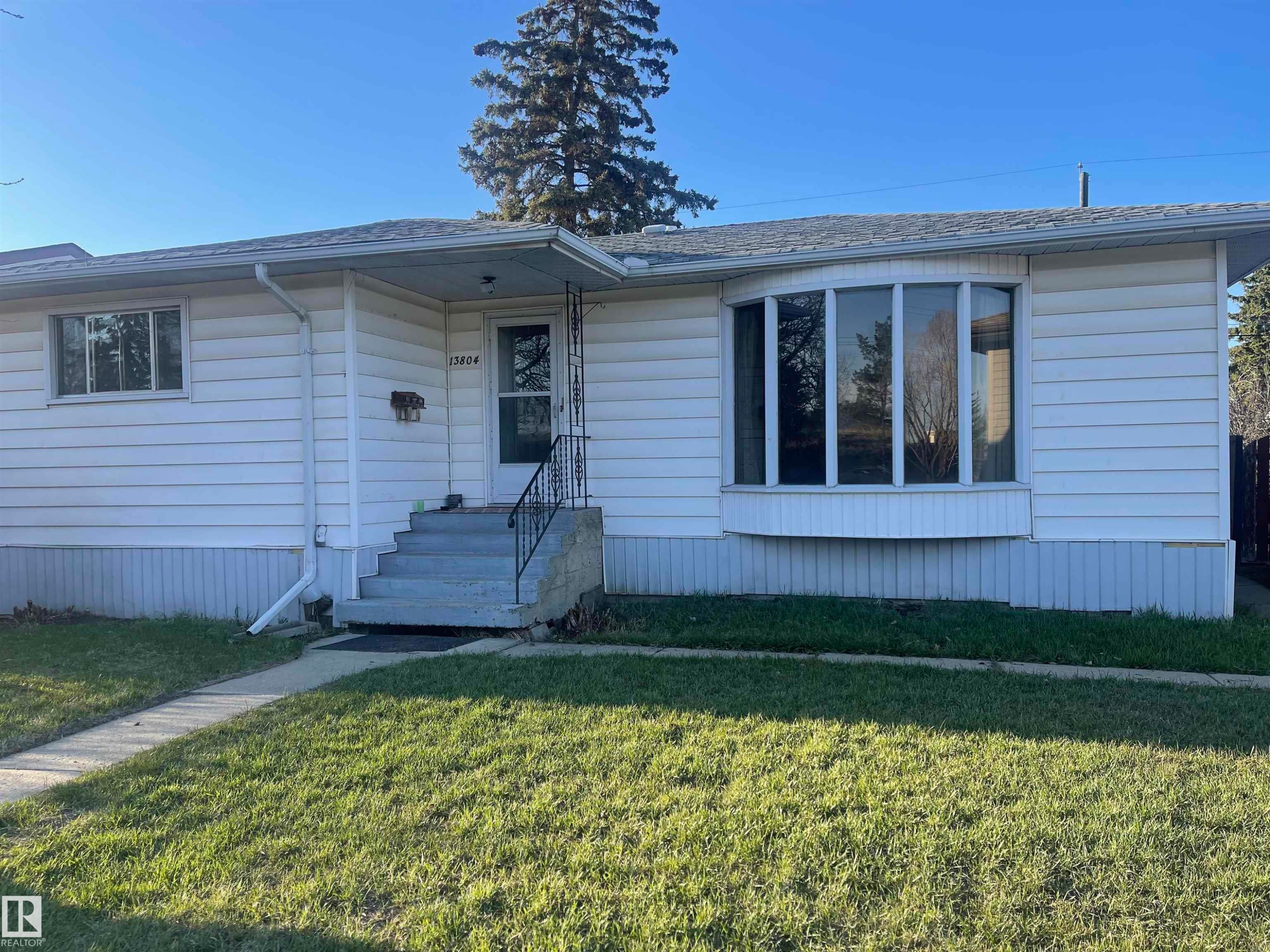 Single-story residence featuring white horizontal siding, a prominent bay window, a concrete walkway, and a covered entry with wrought iron railings - 13804 132 Avenue, Edmonton, AB - Outdoor