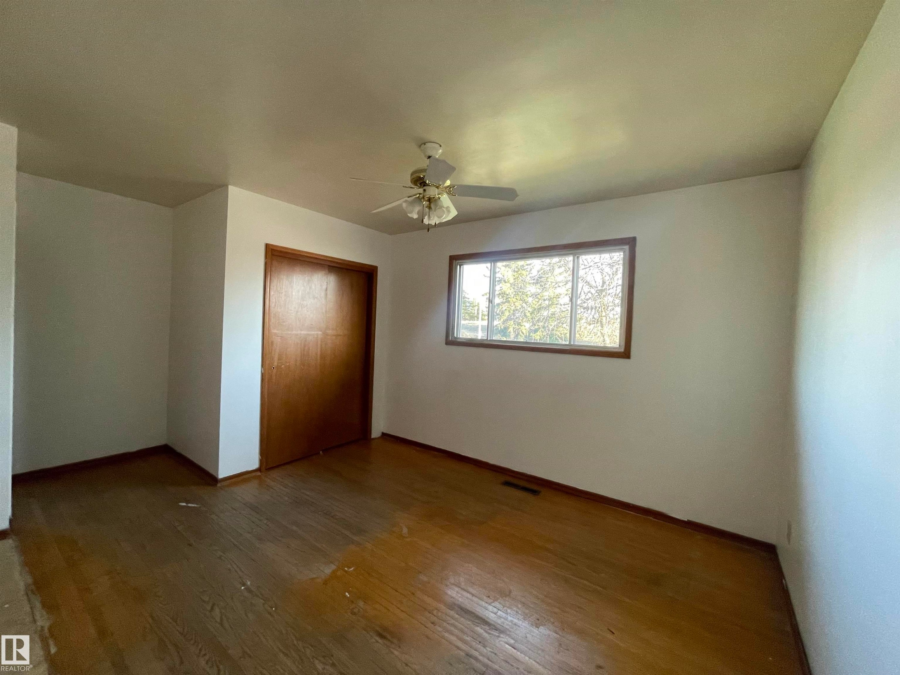 Room featuring wood-finish flooring, a ceiling fan, a window with wood trim, and a built-in closet with sliding wood doors - 13804 132 Avenue, Edmonton, AB - Indoor Photo Showing Other Room