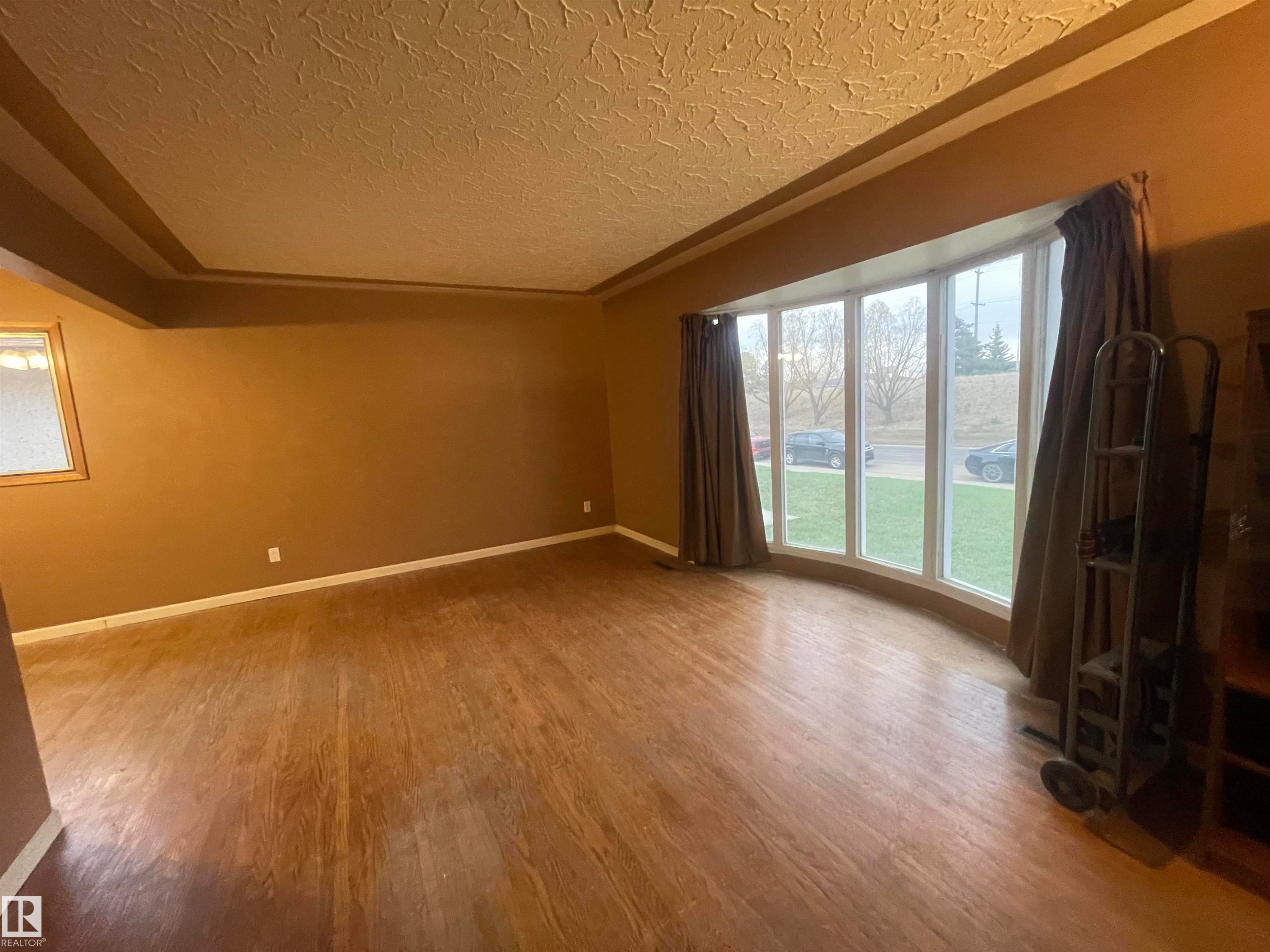 Expansive interior space featuring wood-finish flooring, a tray ceiling, and a large bay window - 13804 132 Avenue, Edmonton, AB - Indoor Photo Showing Other Room