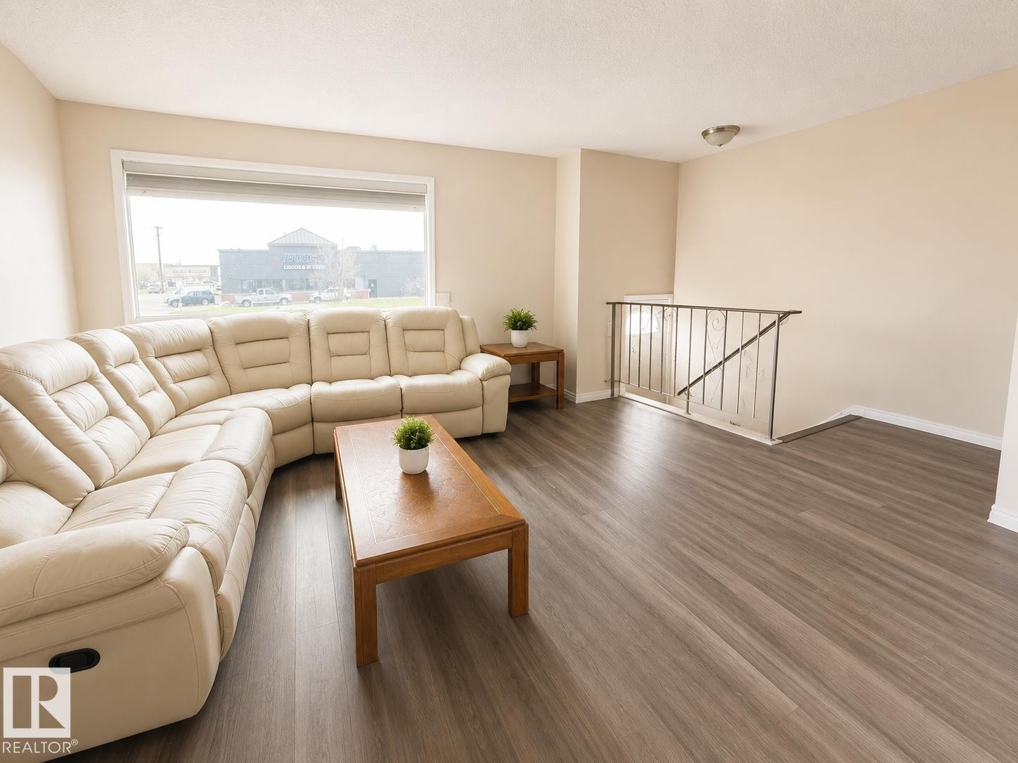 Expansive living area featuring wood-finish flooring, a large picture window, a neutral color palette, and a metal stair railing - 5712 101 Avenue, Edmonton, AB - Indoor Photo Showing Living Room