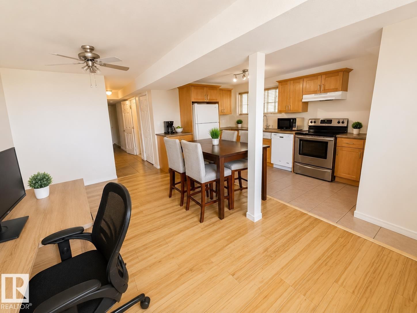 Open-concept living space featuring wood-finish flooring, a ceiling fan, and a kitchen with wood cabinetry, stainless steel appliances, and tile flooring - 5712 101 Avenue, Edmonton, AB - Indoor