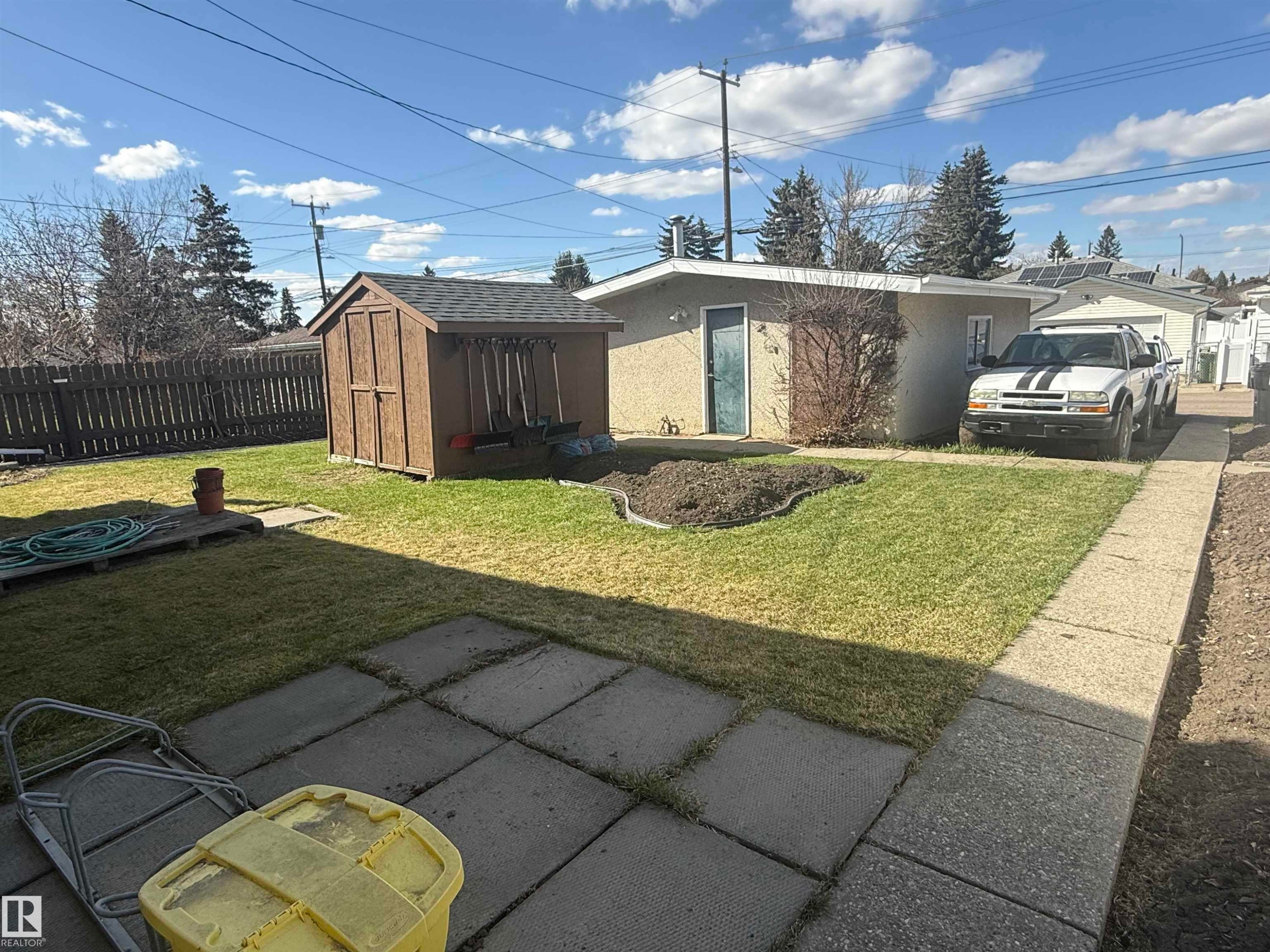 Expansive backyard featuring a manicured lawn, a wood-finish shed with a shingled roof, a paved patio area, and a concrete pathway - 5712 101 Avenue, Edmonton, AB - Outdoor