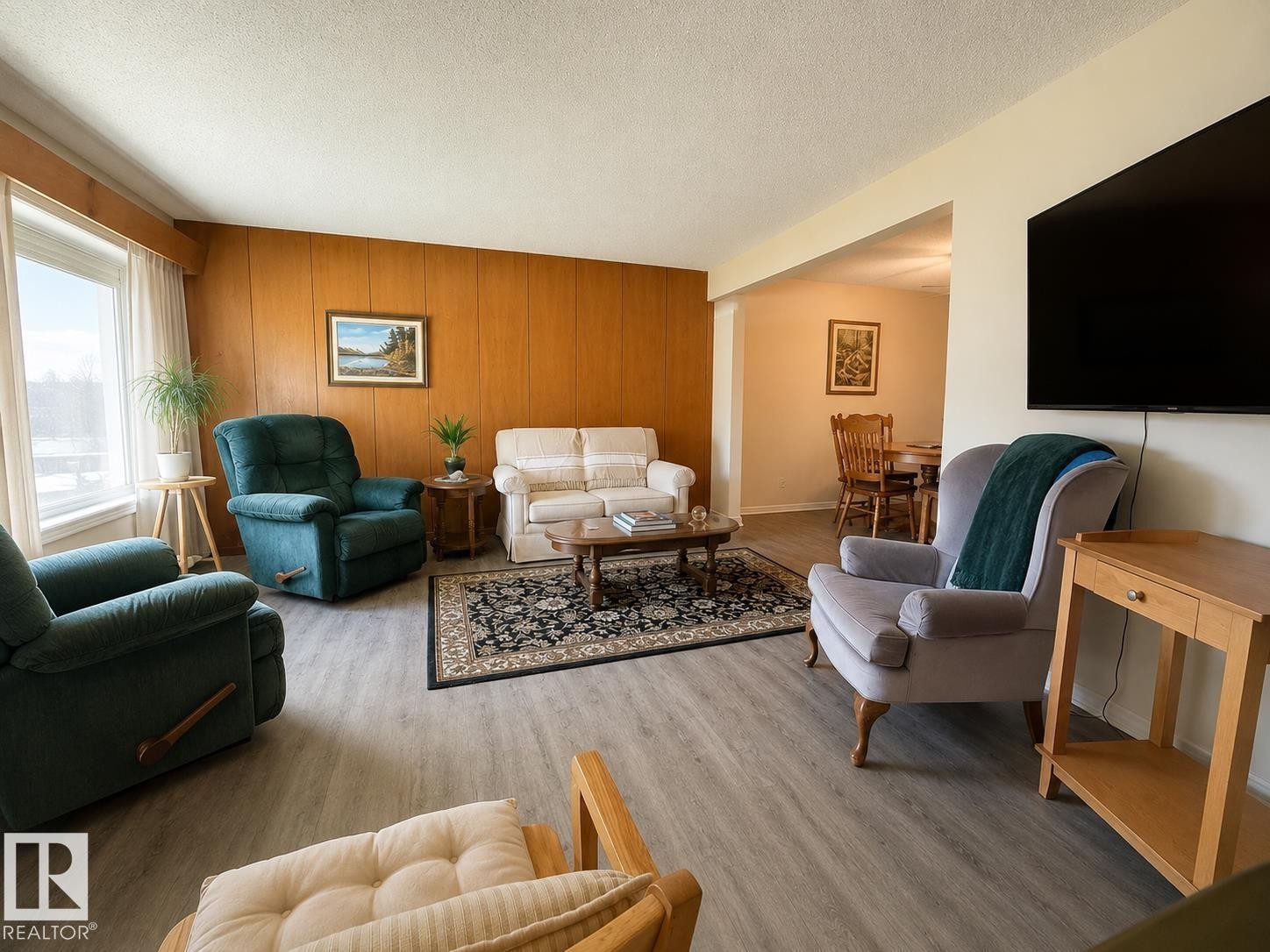 Living area featuring light wood-finish flooring, a wood-paneled accent wall, a large window, and an open entryway to an additional room - 5712 101 Avenue, Edmonton, AB - Indoor Photo Showing Living Room