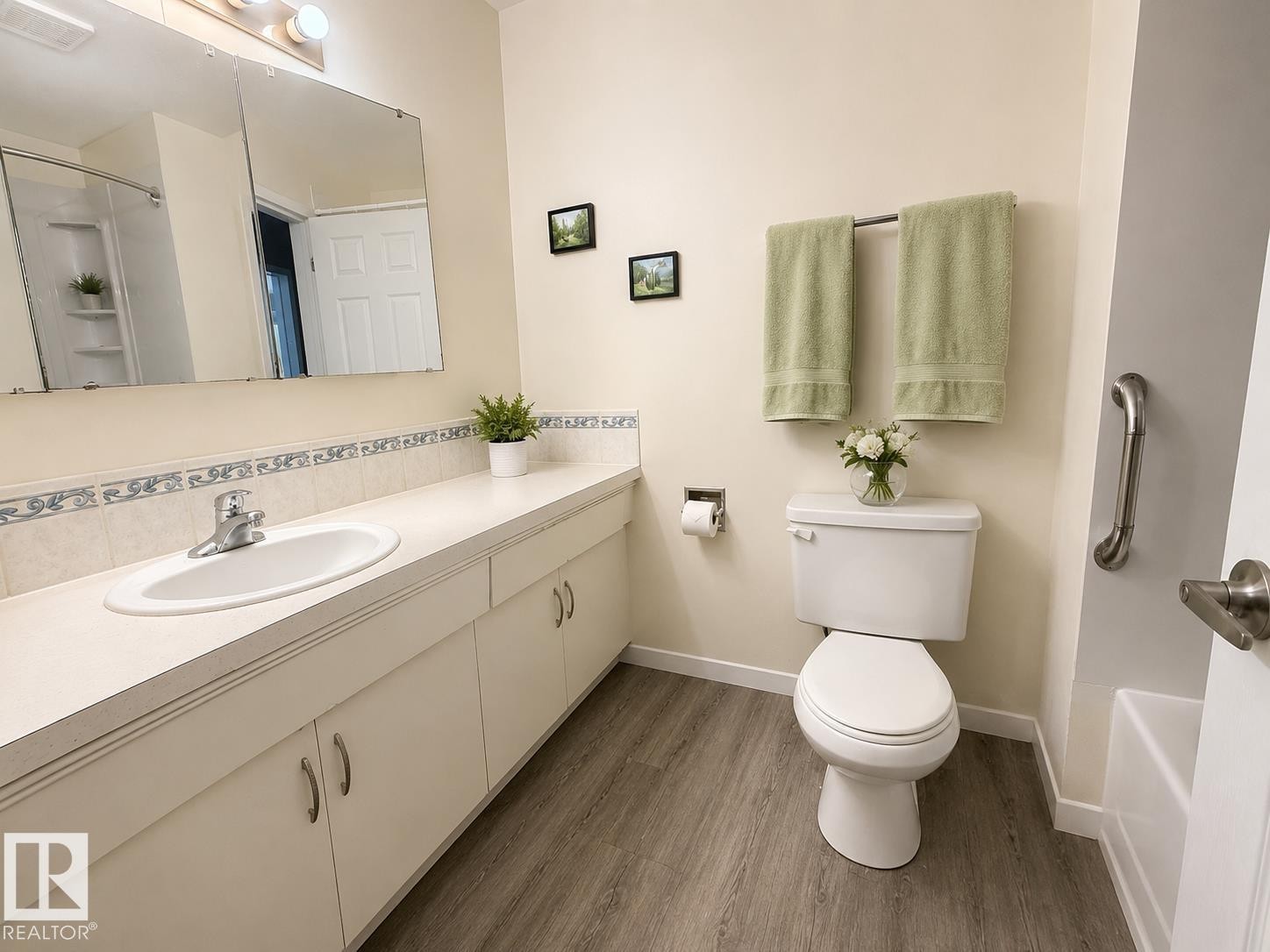 Bathroom featuring a spacious vanity with integrated sink, white cabinetry, wood-finish flooring, and a shower with built-in shelving - 5712 101 Avenue, Edmonton, AB - Indoor Photo Showing Bathroom