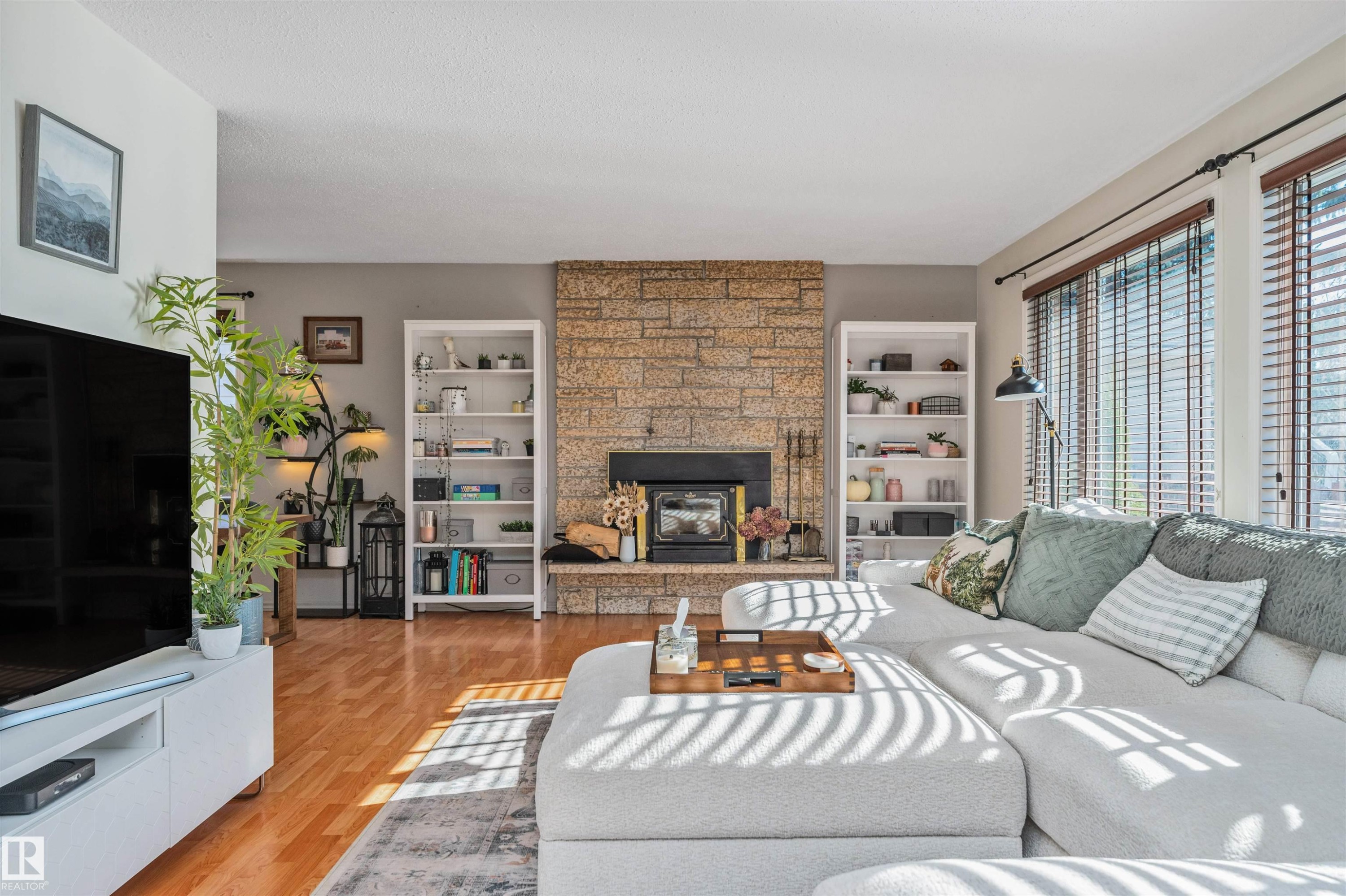 Living area featuring a stone accent wall, wood-finish flooring, and ample natural light from multiple windows - 49 Ash Crescent, St. Albert, AB - Indoor Photo Showing Living Room With Fireplace