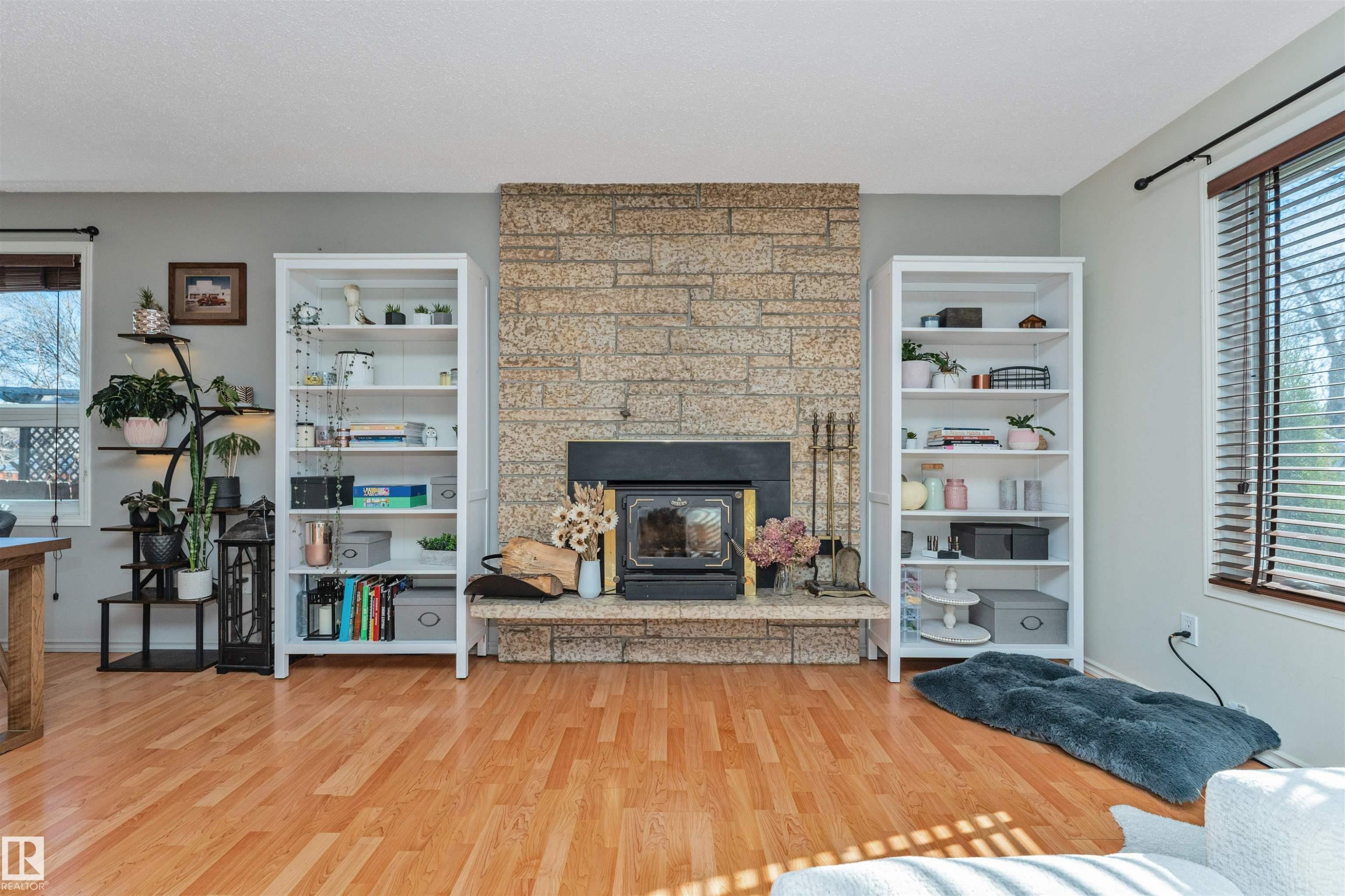 Stone-clad fireplace with a black wood-burning insert, flanked by built-in white shelving units - 49 Ash Crescent, St. Albert, AB - Indoor Photo Showing Living Room With Fireplace