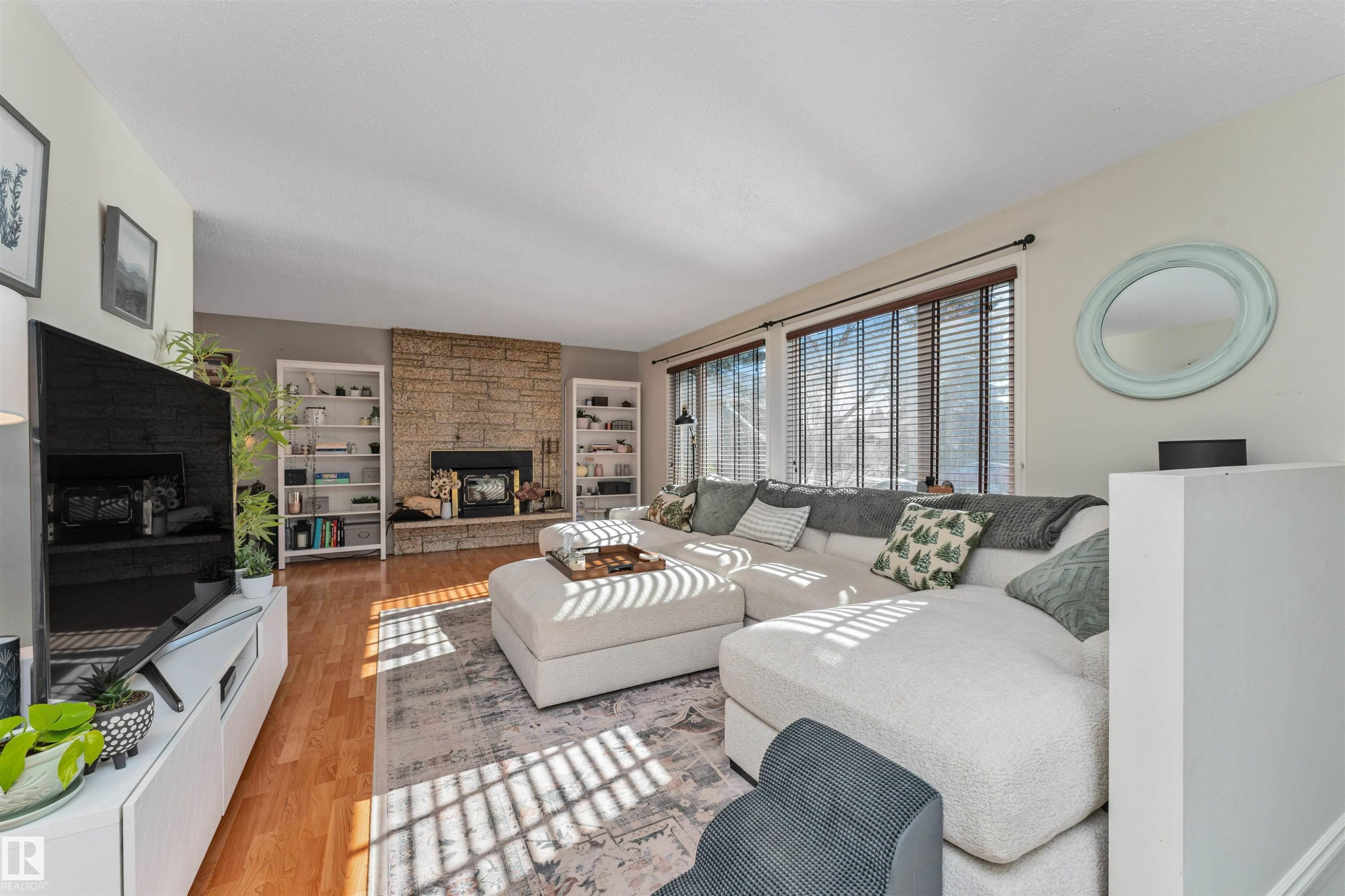 Living area featuring wood-finish flooring, a stone-clad fireplace, and twin built-in shelving units - 49 Ash Crescent, St. Albert, AB - Indoor Photo Showing Living Room With Fireplace