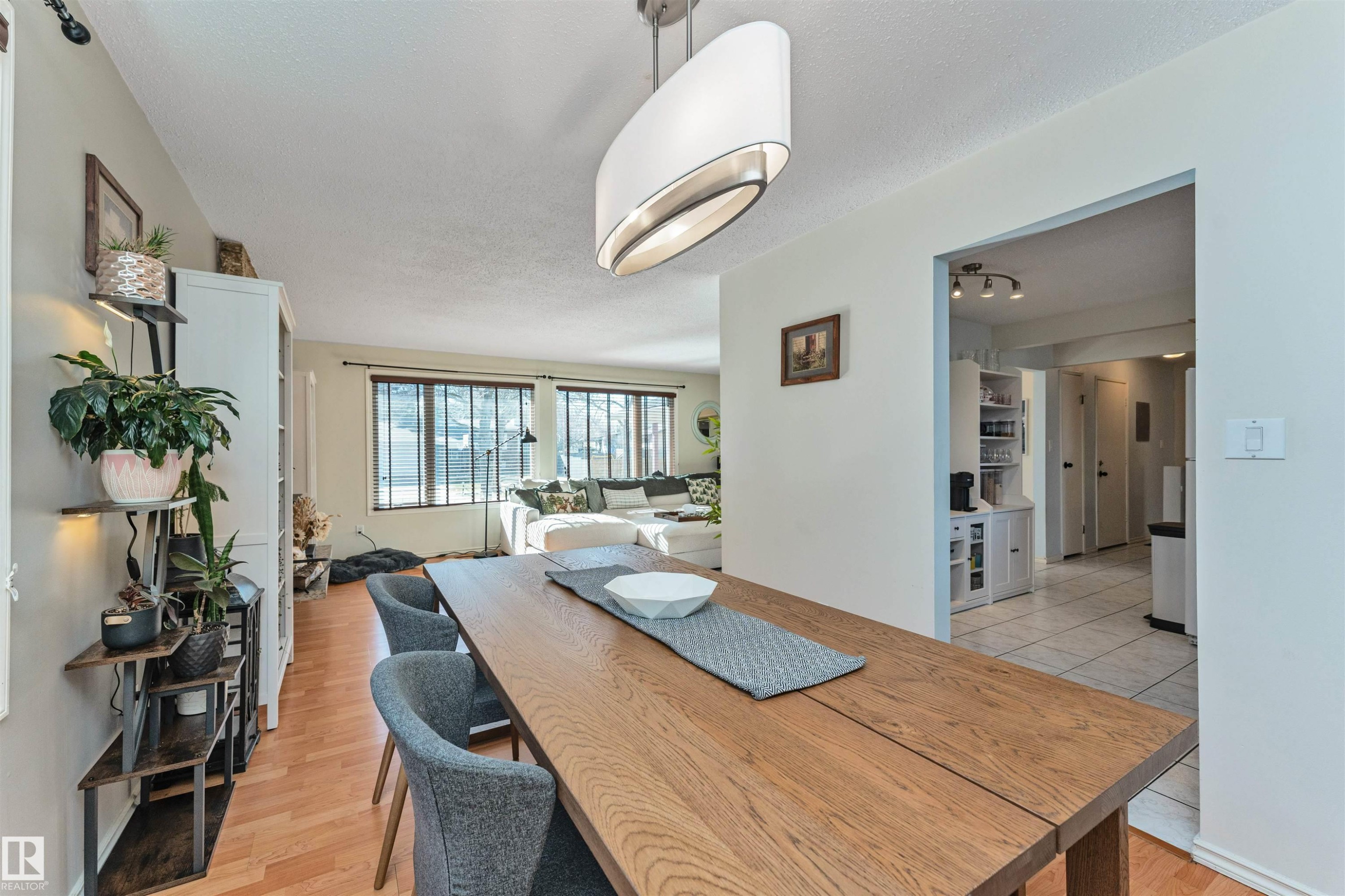 Dining area featuring wood-finish flooring, a contemporary oval pendant light fixture, and an open entryway to an additional living space with large windows - 49 Ash Crescent, St. Albert, AB - Indoor
