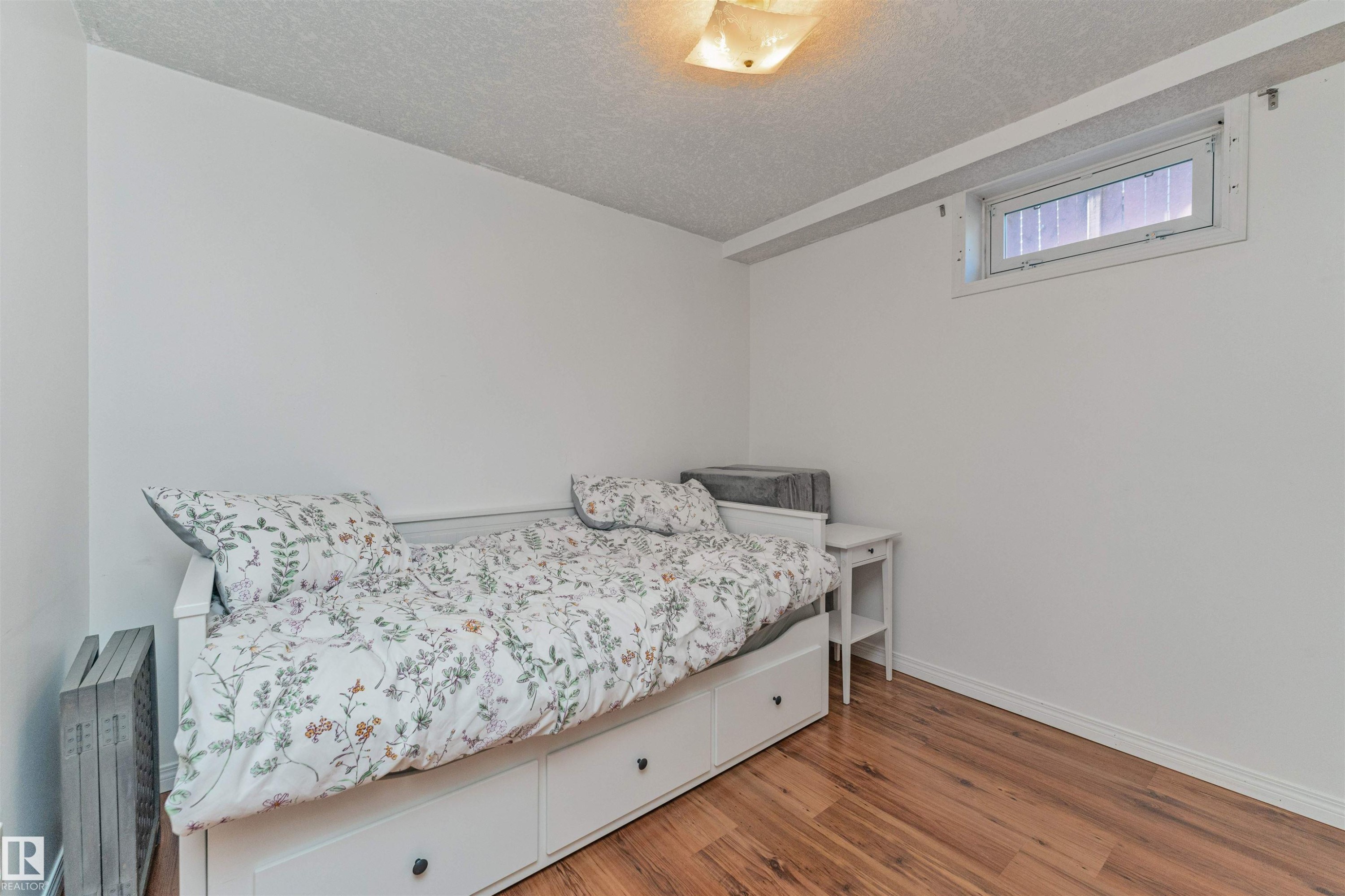 Interior room featuring wood-finish flooring, white walls, and a single basement window - 49 Ash Crescent, St. Albert, AB - Indoor Photo Showing Bedroom