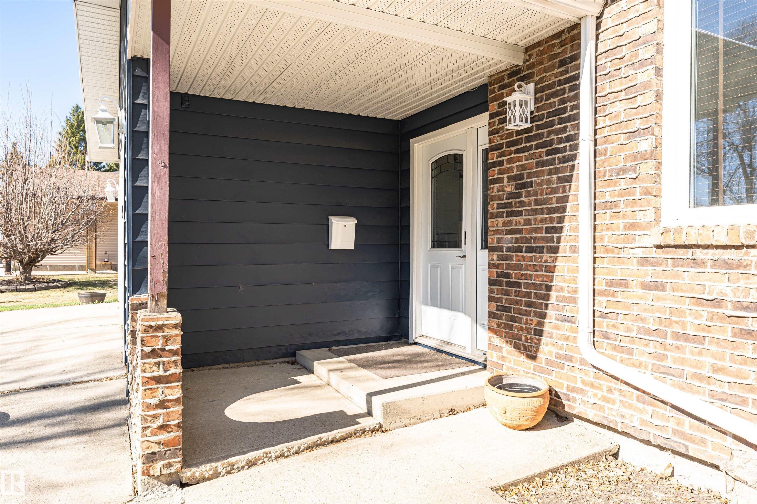 Covered front entry featuring a white paneled door with arched glass insert, exterior wall lantern, and concrete steps - 49 Ash Crescent, St. Albert, AB - Outdoor With Exterior