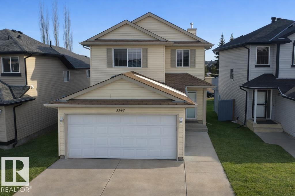 The property features a two-story exterior with light-colored siding, a garage with a driveway, and a well-maintained lawn - 3347 24 Avenue, Edmonton, AB - Outdoor With Facade