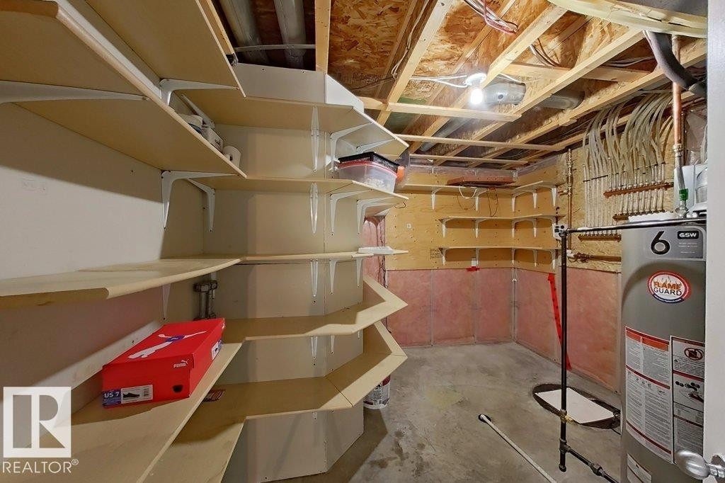 The property features an unfinished basement with extensive built-in shelving, exposed ceiling joists and plumbing, and a water heater - 3347 24 Avenue, Edmonton, AB - Indoor Photo Showing Basement