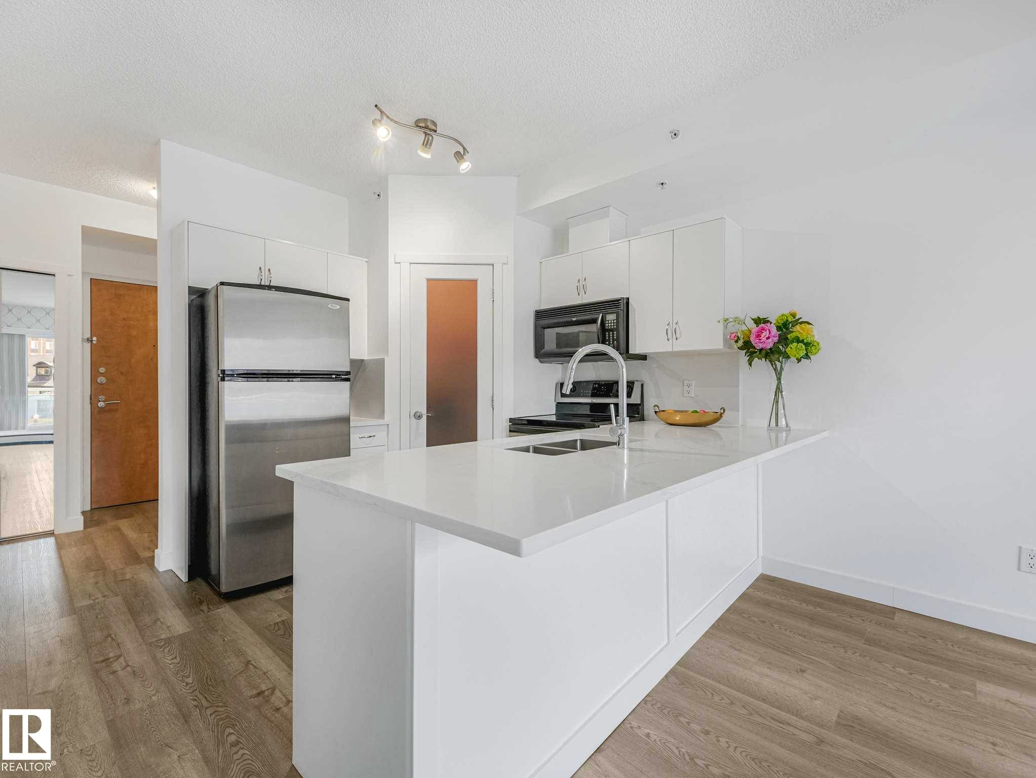 Kitchen featuring white cabinetry, stainless steel appliances, a center island with an integrated sink, and wood-finish flooring - 305 10504 99 Avenue, Edmonton, AB - Indoor Photo Showing Kitchen With Double Sink With Upgraded Kitchen