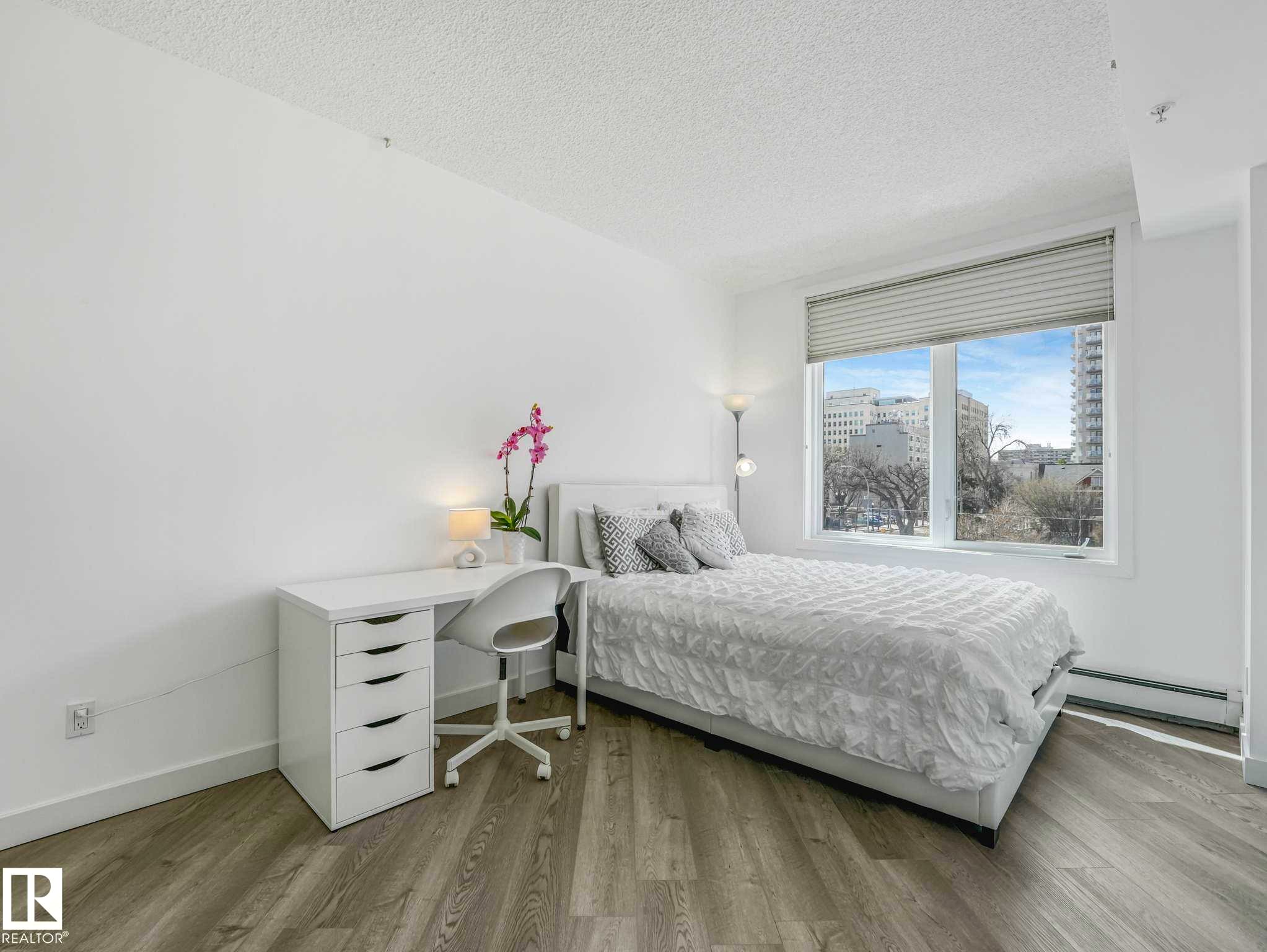 Bright interior space featuring wood-finish flooring, white baseboards, and a large window with horizontal blinds - 305 10504 99 Avenue, Edmonton, AB - Indoor Photo Showing Bedroom