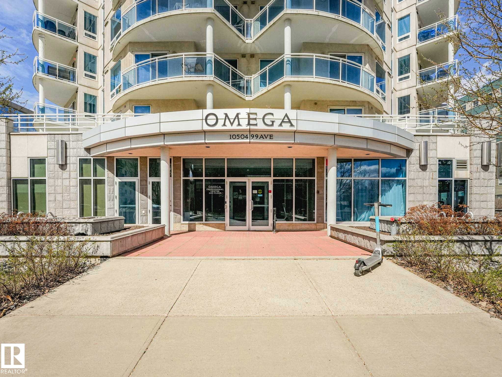 Building exterior featuring multiple balconies with glass railings, a curved entrance canopy, large storefront windows, and a stone facade - 305 10504 99 Avenue, Edmonton, AB - Indoor
