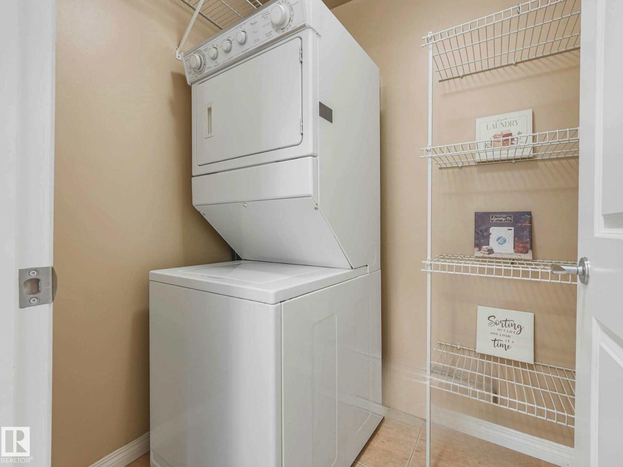 Dedicated laundry area featuring a stacked washer and dryer unit, wire shelving, and neutral wall paint - 305 10504 99 Avenue, Edmonton, AB - Indoor Photo Showing Laundry Room