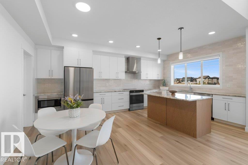 Modern kitchen featuring white cabinetry, stainless steel appliances, a center island with pendant lighting, and light wood-finish flooring - 19110 20A Avenue, Edmonton, AB - Indoor
