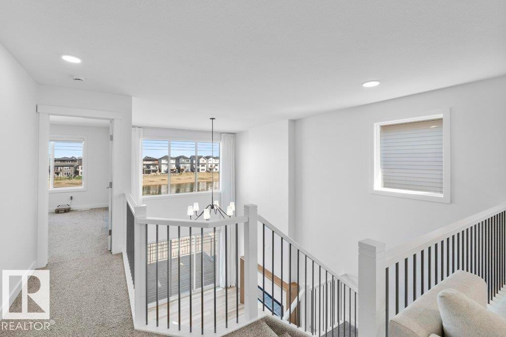 Upper landing featuring a modern black chandelier, white painted balusters, black metal railings, recessed lighting, and expansive windows - 19110 20A Avenue, Edmonton, AB - Indoor Photo Showing Other Room