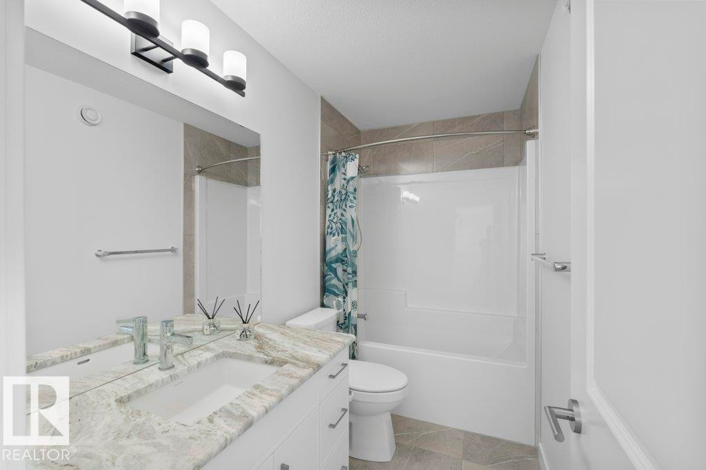 Bathroom featuring a white vanity with double sinks, a patterned stone countertop, and an integrated tub-shower combination with tiled surround - 19110 20A Avenue, Edmonton, AB - Indoor Photo Showing Bathroom