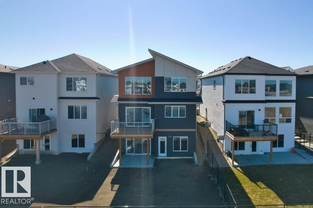 Modern multi-story property featuring a distinctive angular roofline, a combination of dark gray and wood-finish siding, multiple balconies with white railings, a ground-level patio, and a spacious backyard - 19110 20A Avenue, Edmonton, AB - Outdoor With Facade